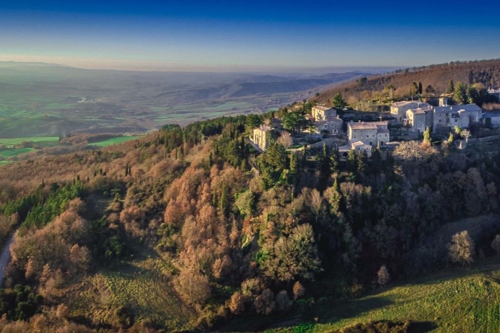 aerial shot of a Tuscan hilltown with a cluster of stone buildings surrounded by a valley below