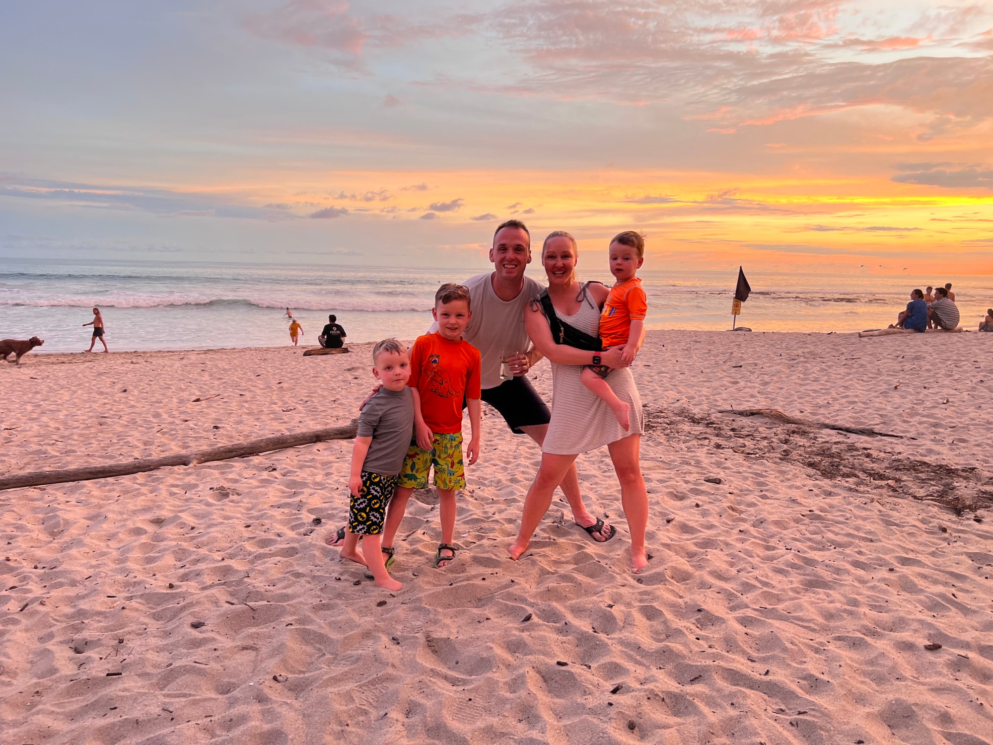 Family of five standing on the beach at sunset under a yellow and orange sky.