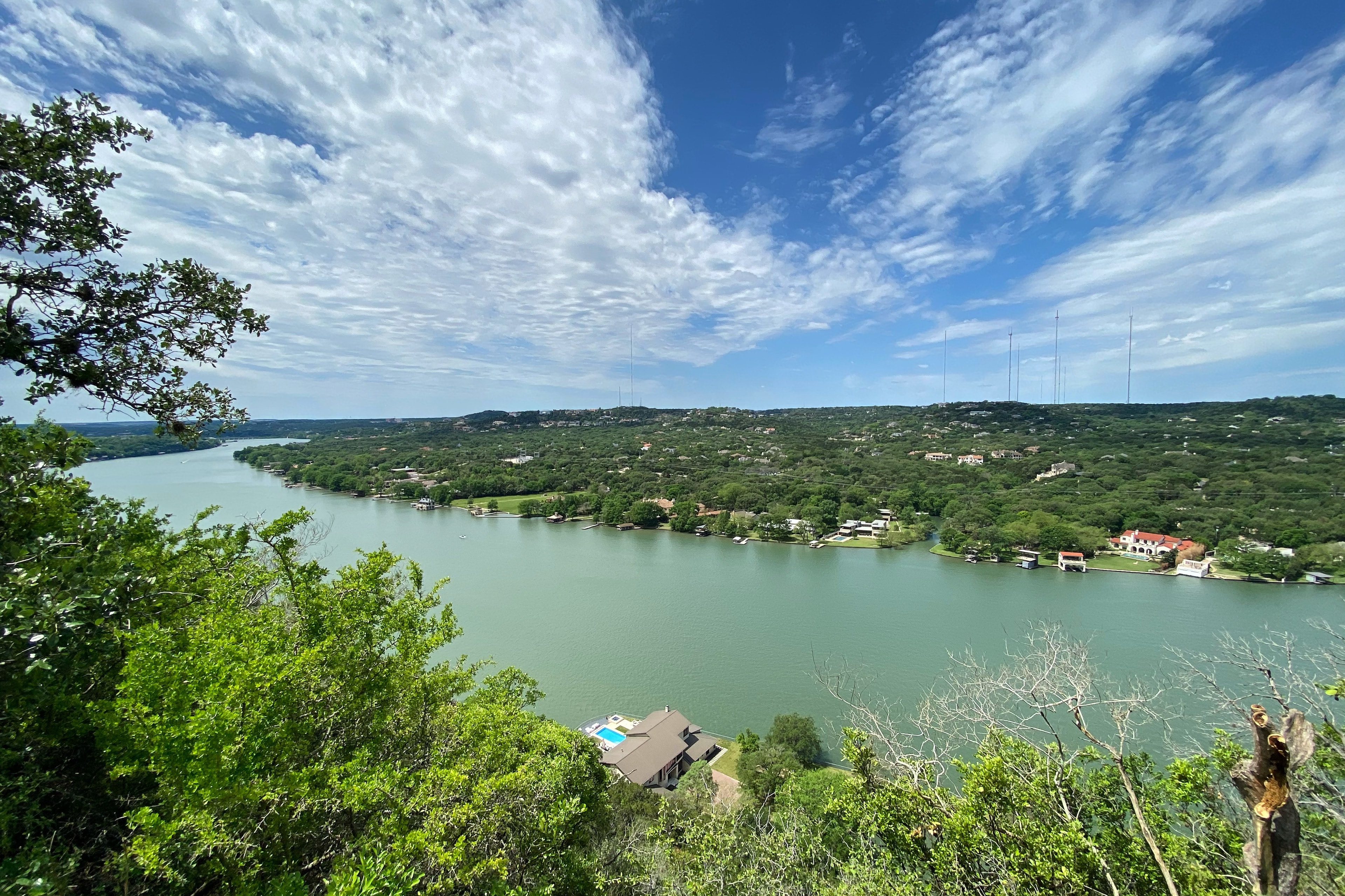 Hike Mount Bonnell to see a beautiful panoramic view of the river surrounding by lush foliage on a clear day with wisps of clouds.