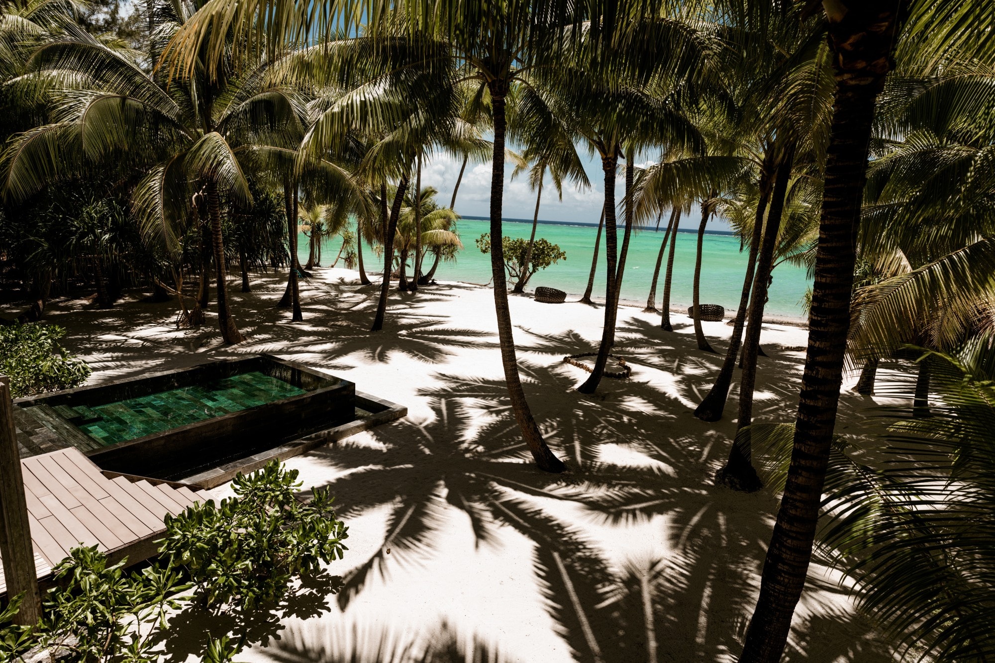 a small plunge pool on a beach strewn with palm trees