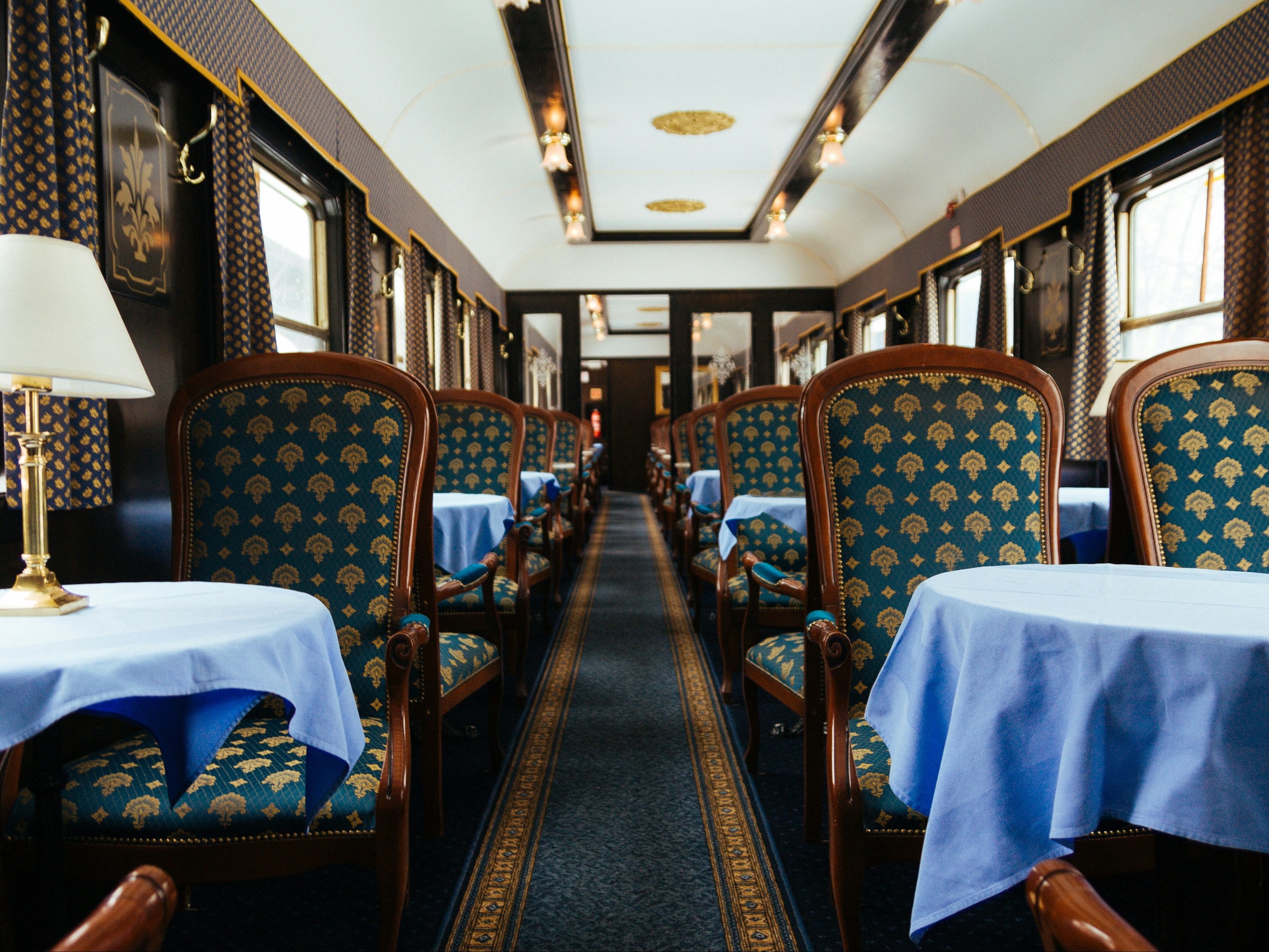 The image depicts the luxurious interior of a vintage train car with elegant seating and dining arrangements.