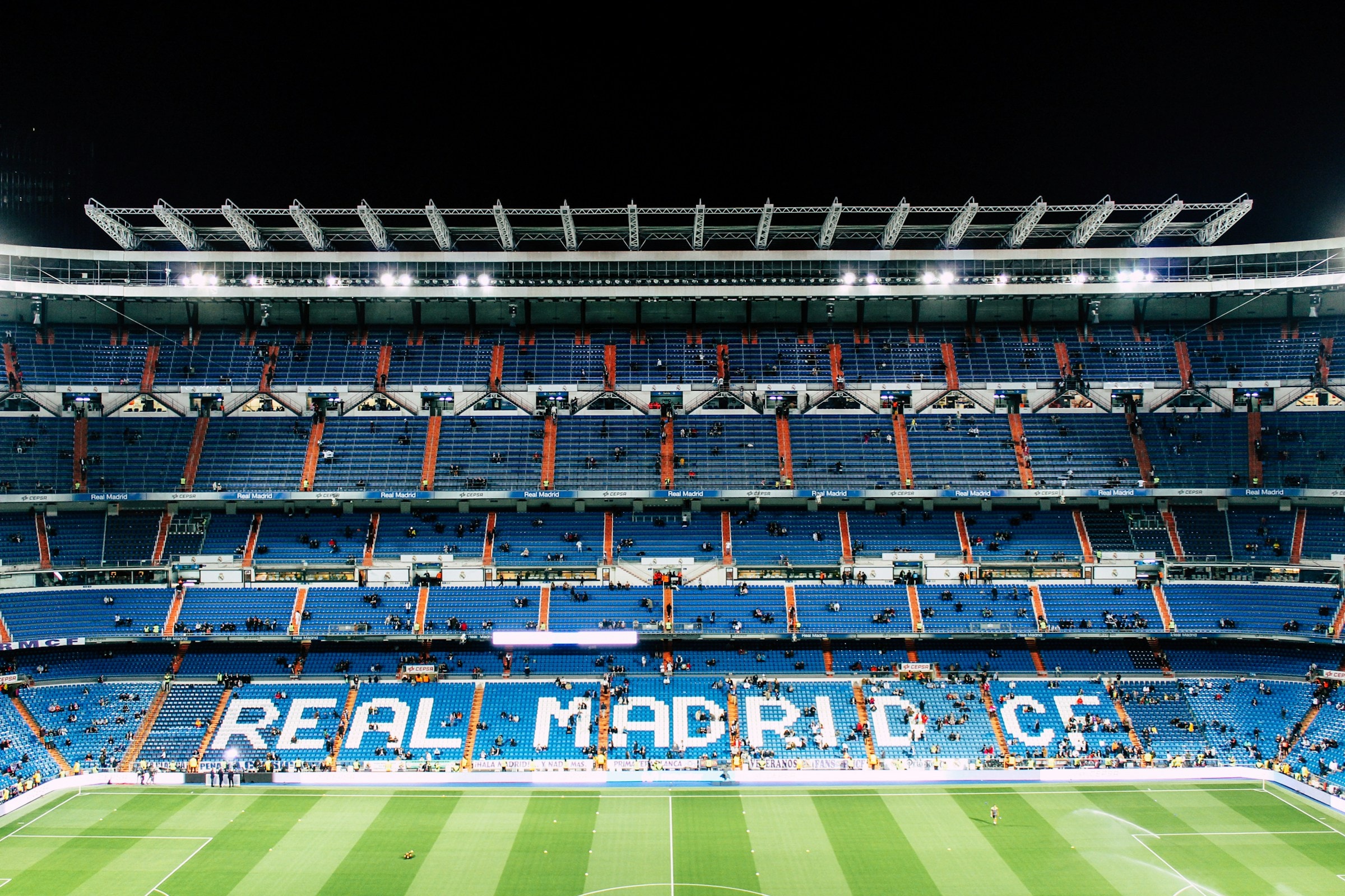 Santiago Bernabeu Stadium in Madrid Spain with blue bleachers and a green field and a few people in the stands.