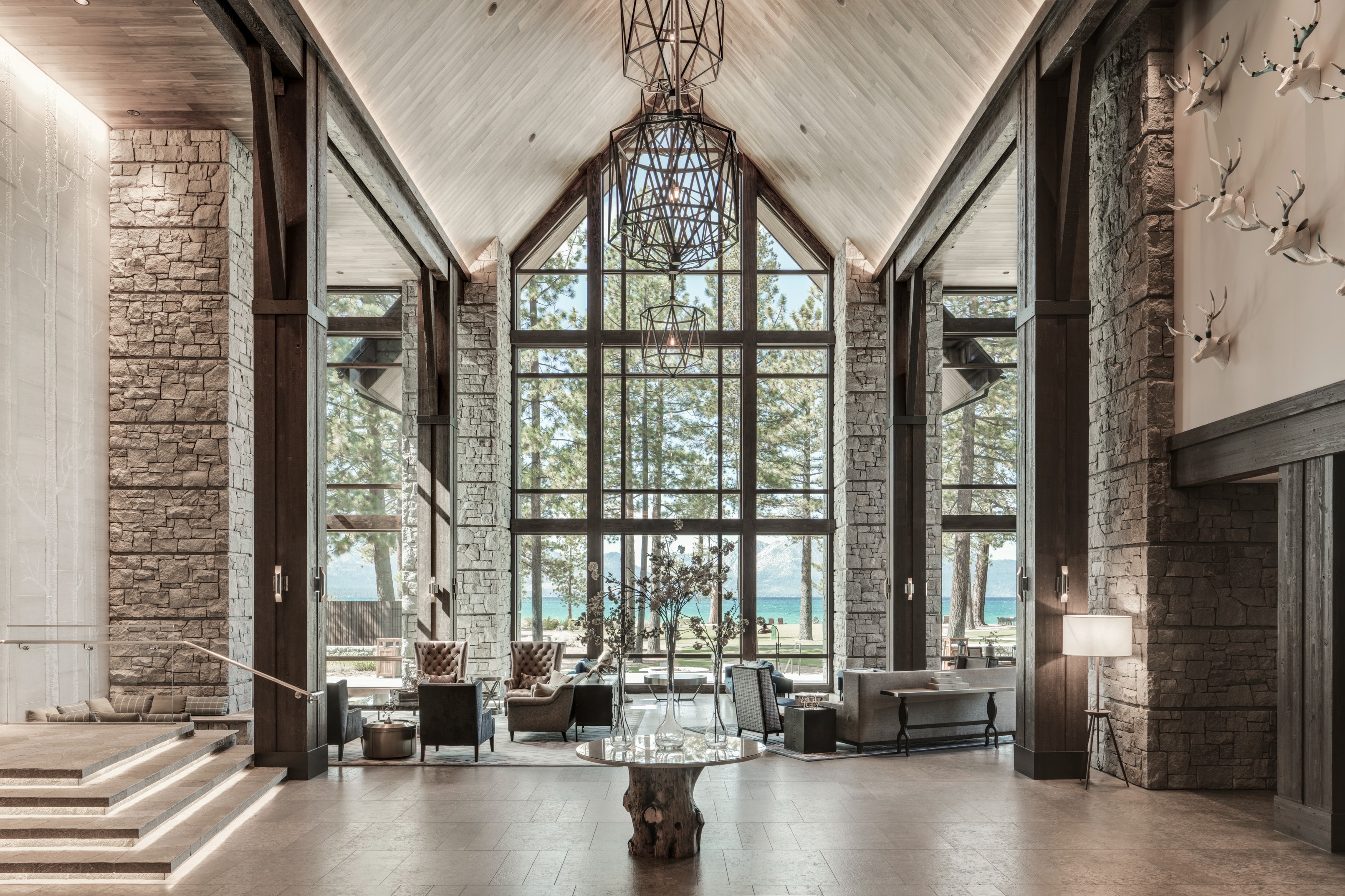 a fancy hotel lobby with towering windows framing mountain trees and a large lake