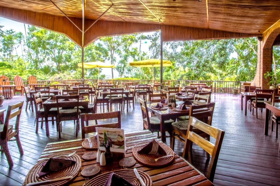 A large wooden outdoor patio with wooden chairs at Heaven Restaurant, with trees in the distance.