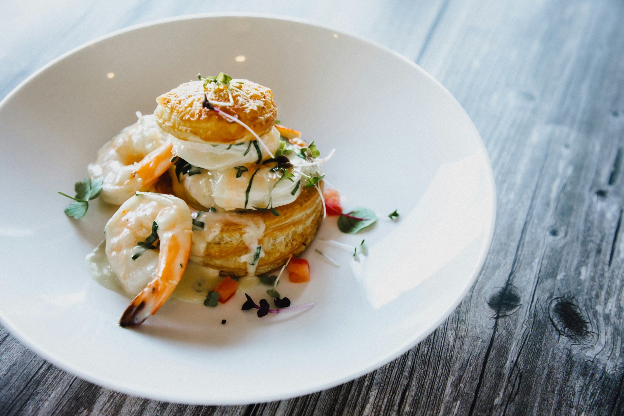 Prawns tower drizzled with white sauce in a white dish on a wooden table.