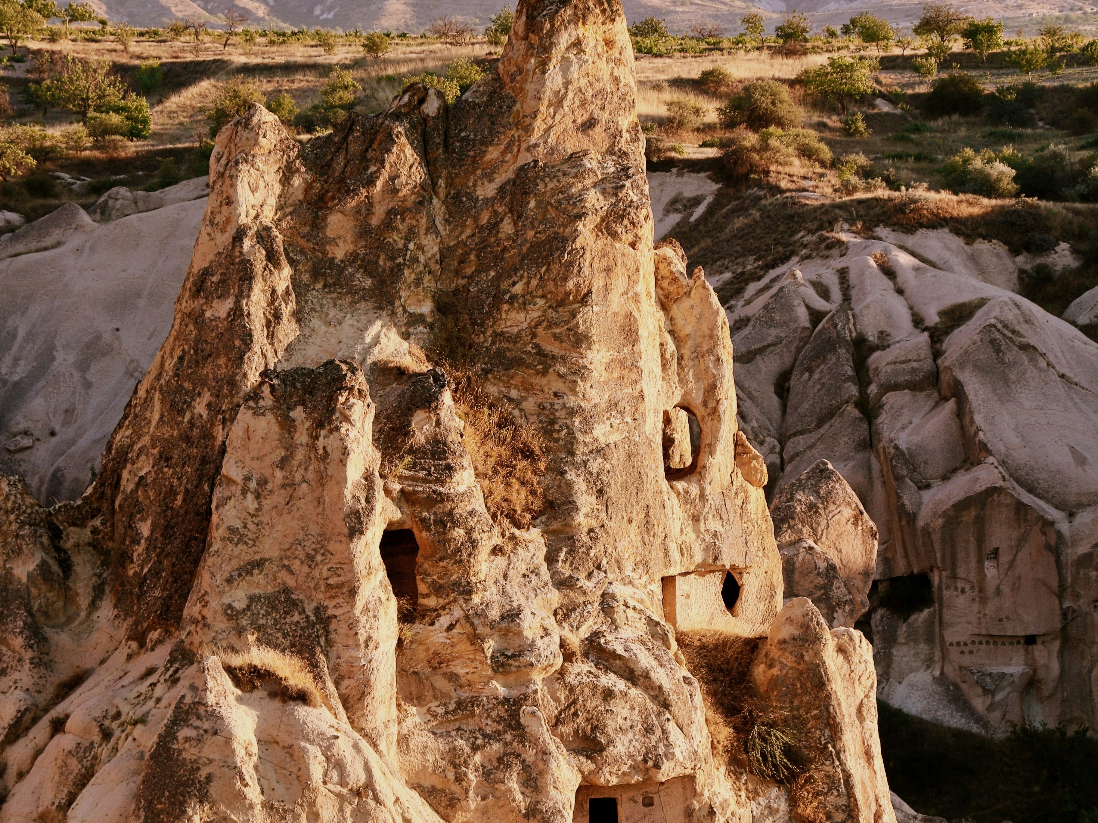 A weathered rock formation with carved openings, reminiscent of ancient dwellings under a clear sky.