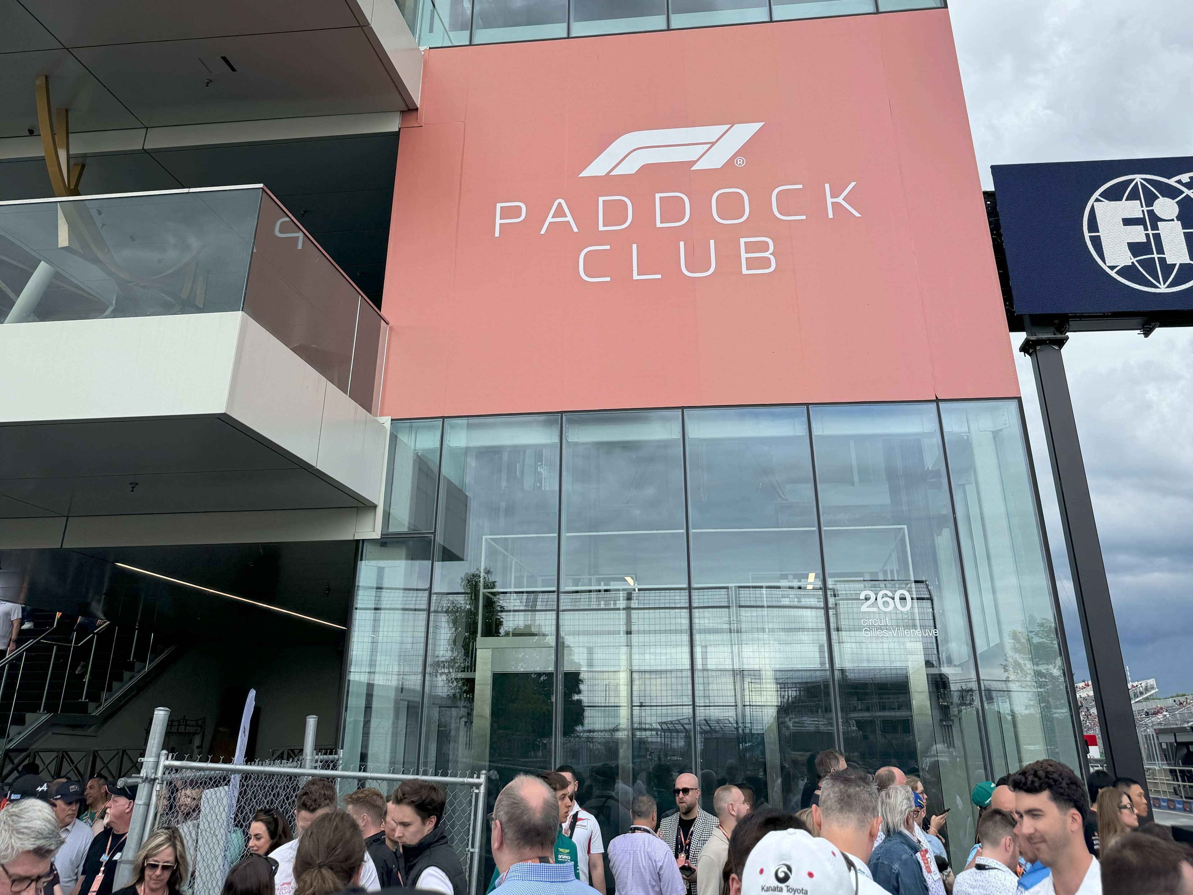 The image captures the essence of anticipation and camaraderie at the “F1 PADDOCK CLUB,” set against a backdrop of an overcast sky.