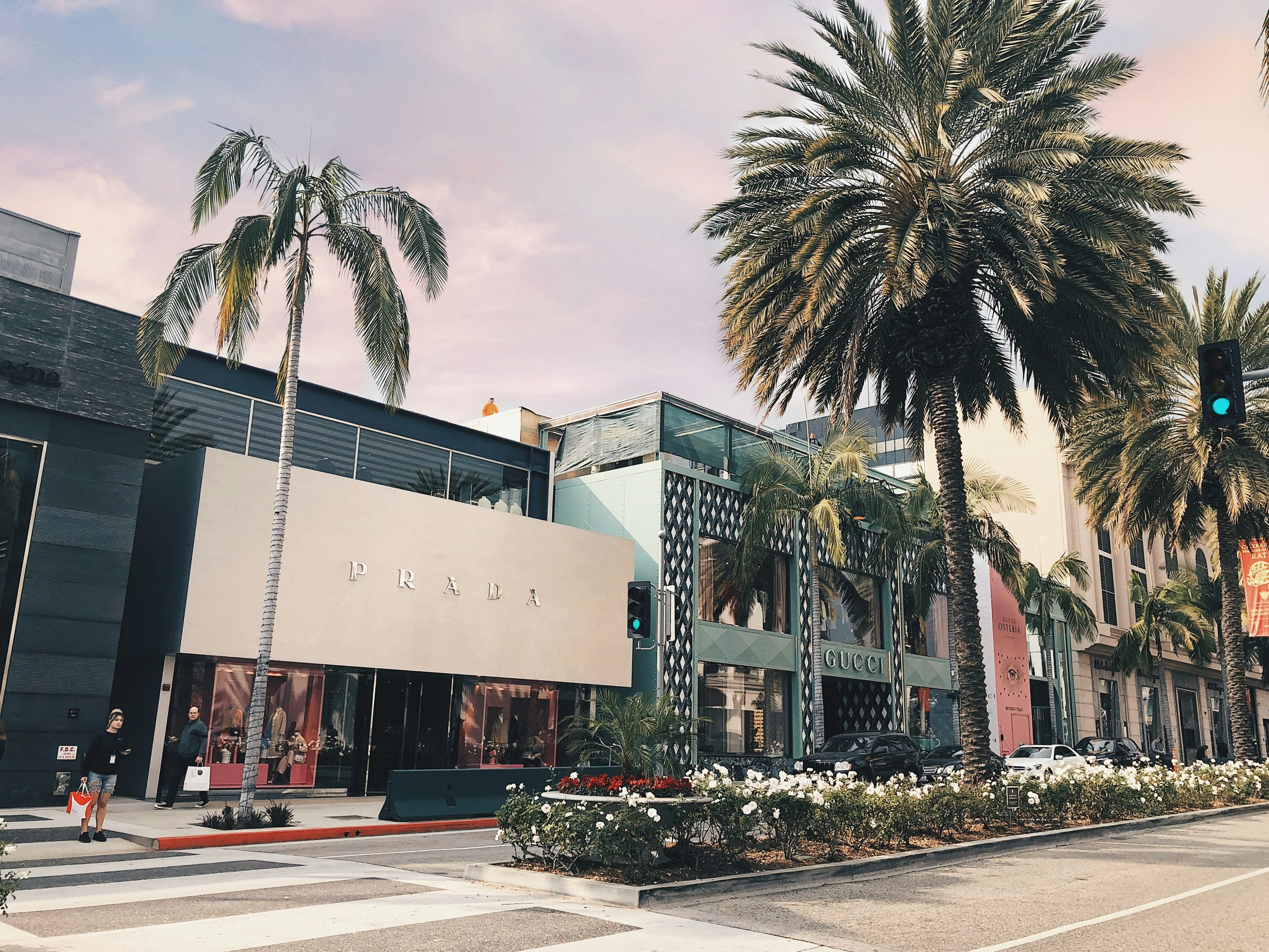 The image captures a street view featuring palm trees, a crosswalk, and the Prada storefront.