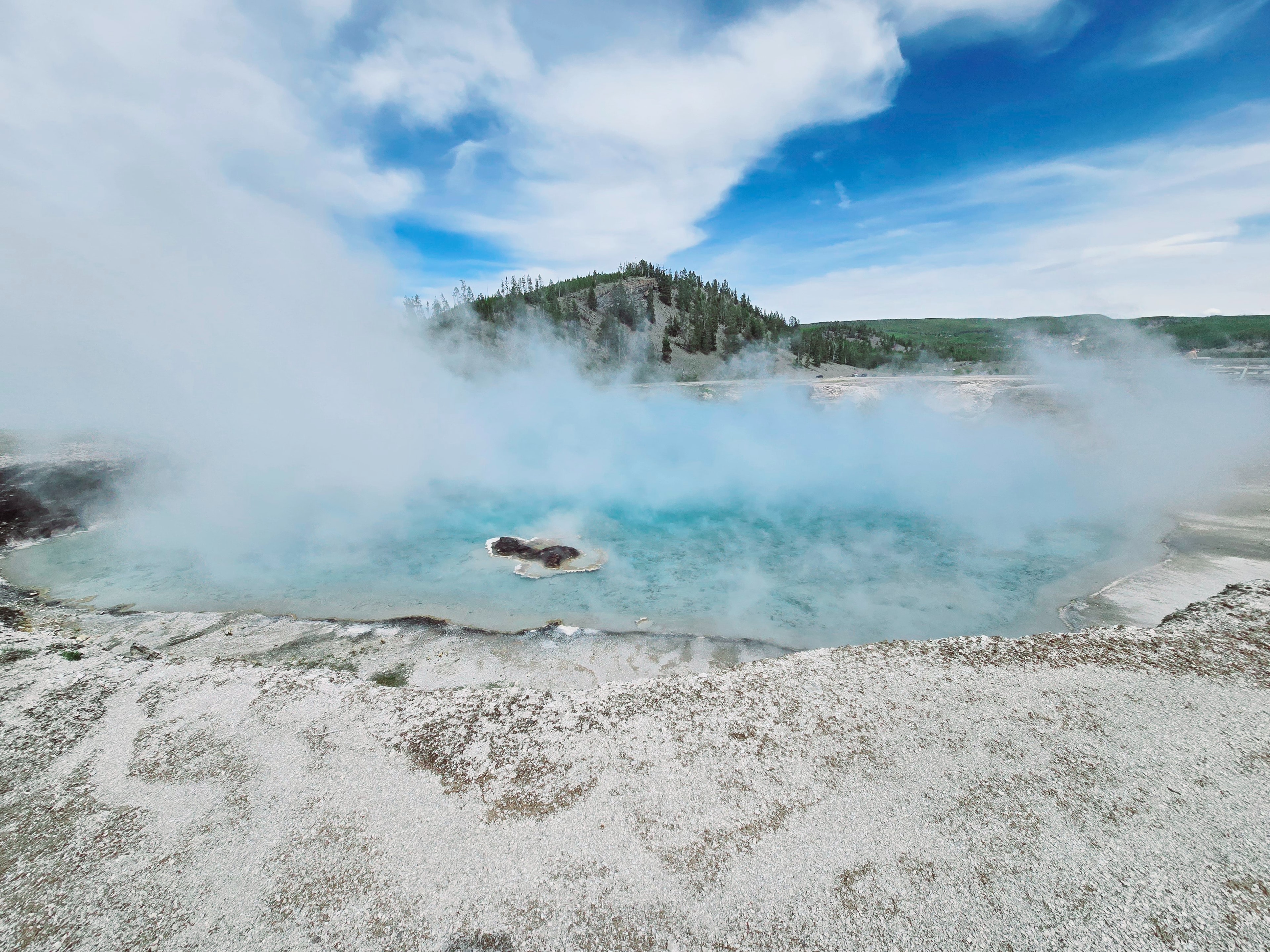 A geothermal spectacle: steam rises from a turquoise hot spring, cradled by a rocky embrace under the open sky.