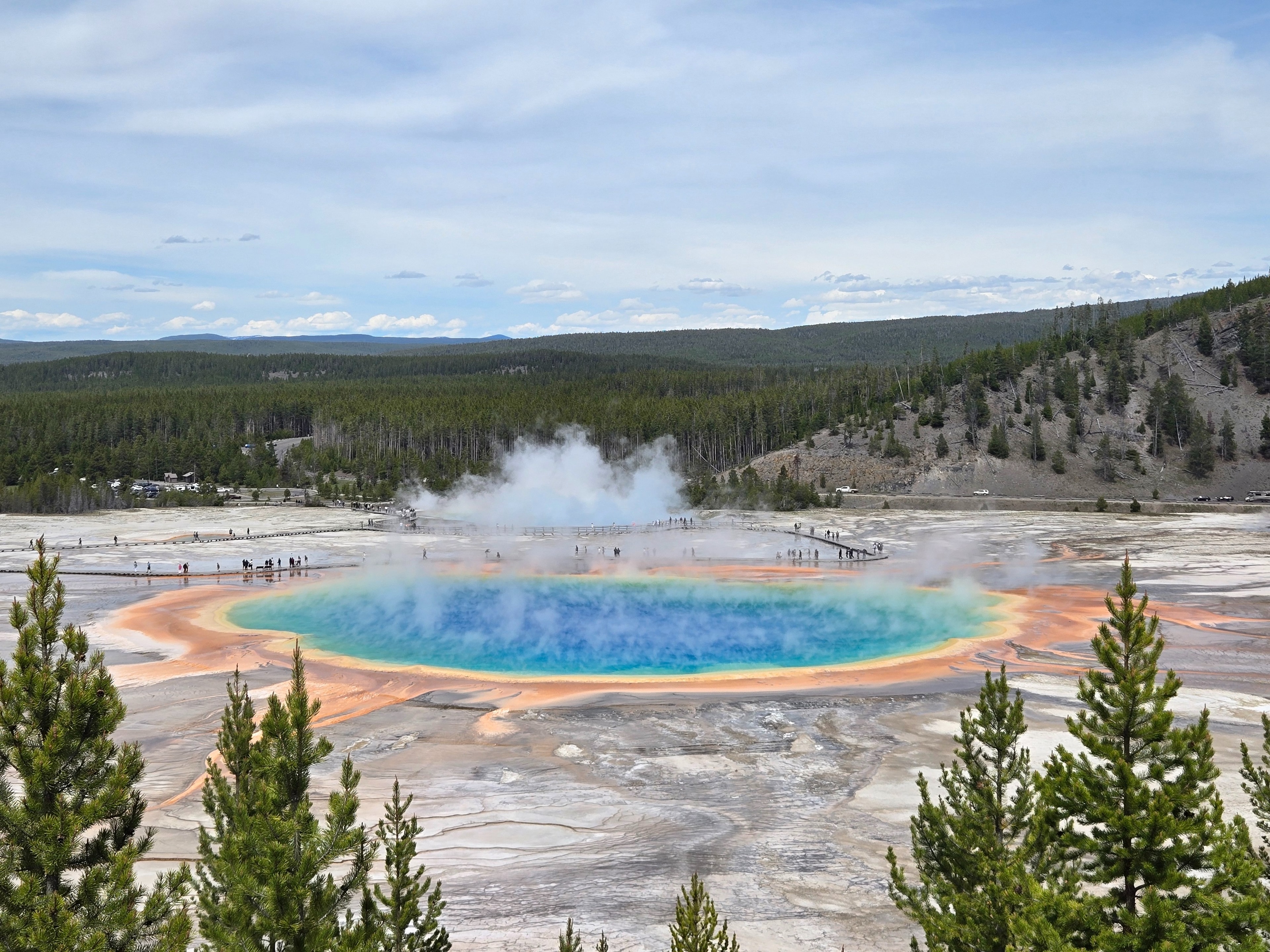 The Grand Prismatic Spring in Yellowstone, a mesmerizing blend of natural colors and steam, captured with a scenic backdrop.