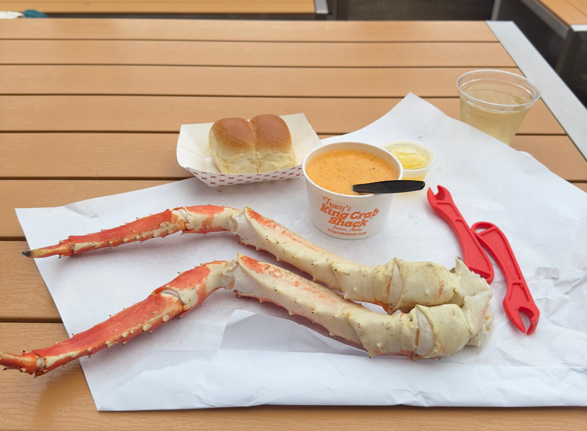 A crab leg on a picnic table with a cup of soup and plate of bread.