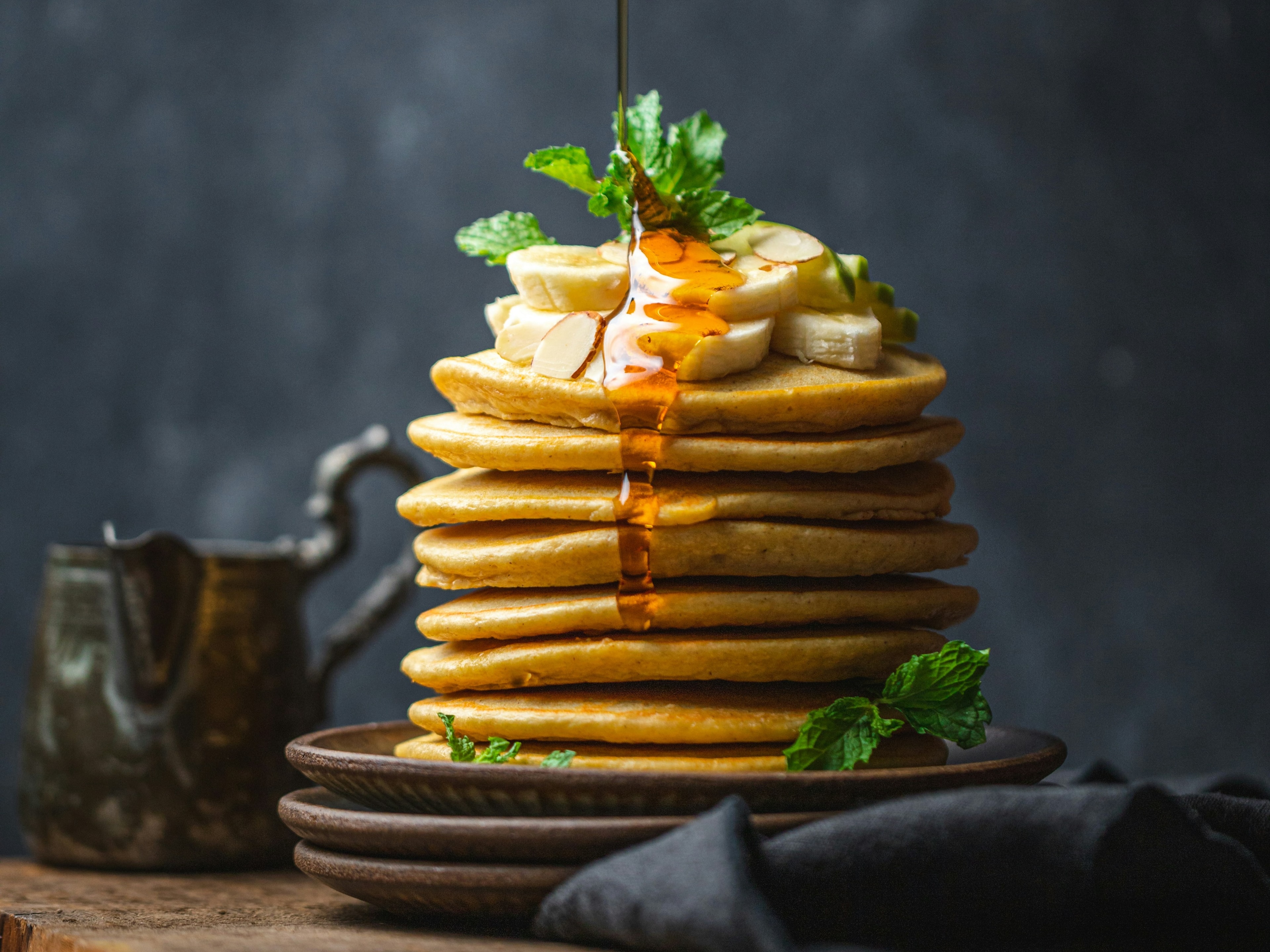 A delightful breakfast scene with pancakes, banana slices, and syrup in mid-pour