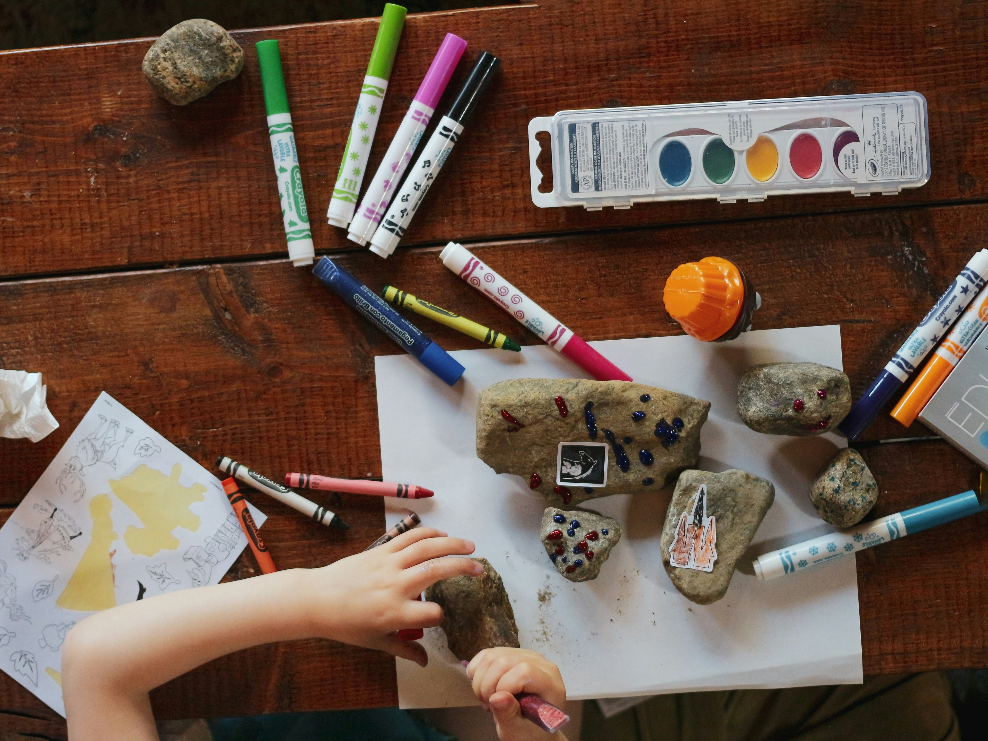 A creative child’s hands busily engaged in painting colorful designs on rocks. 