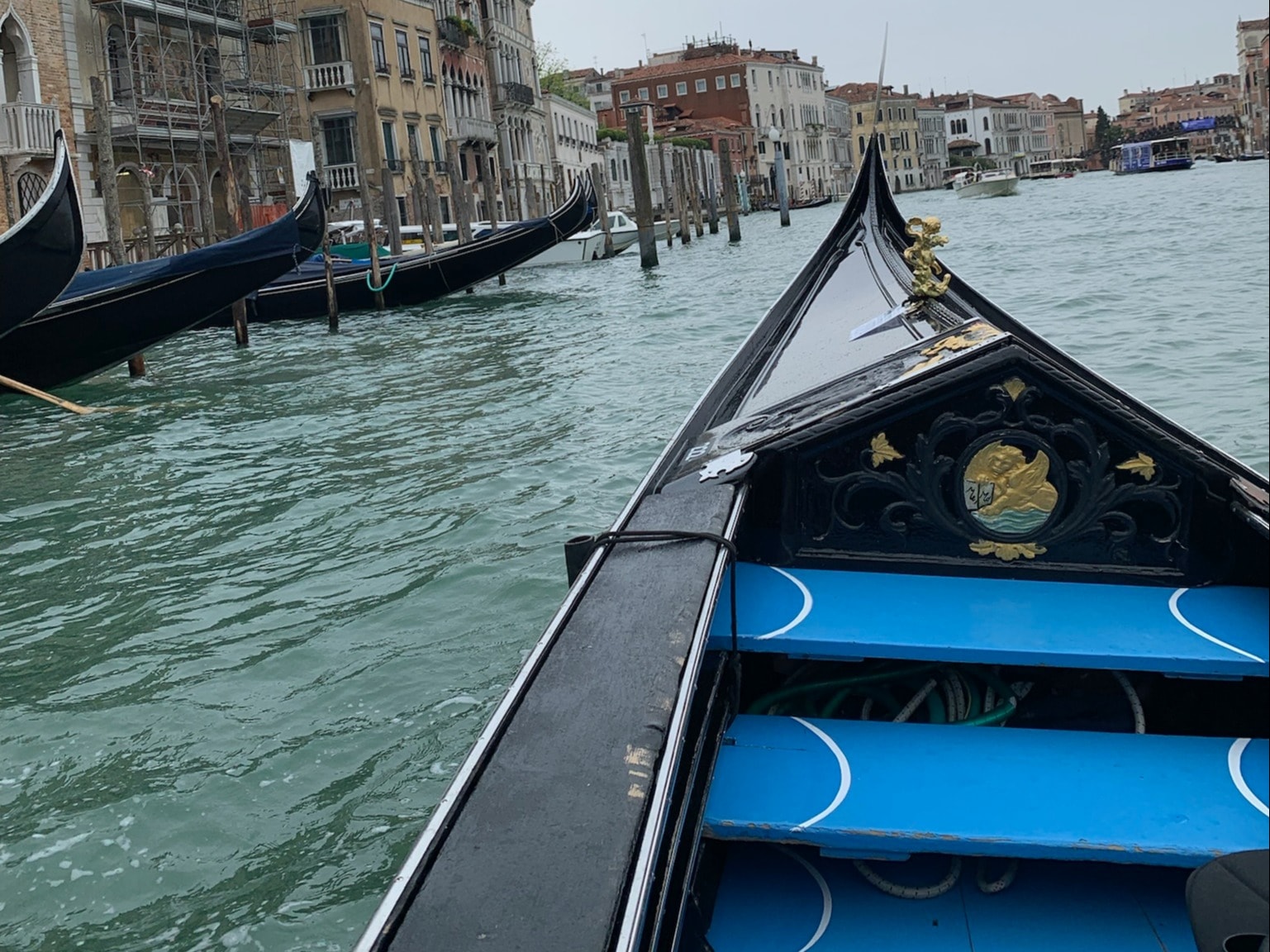 A gondola with blue benches in a Venice canal with buildings along it.