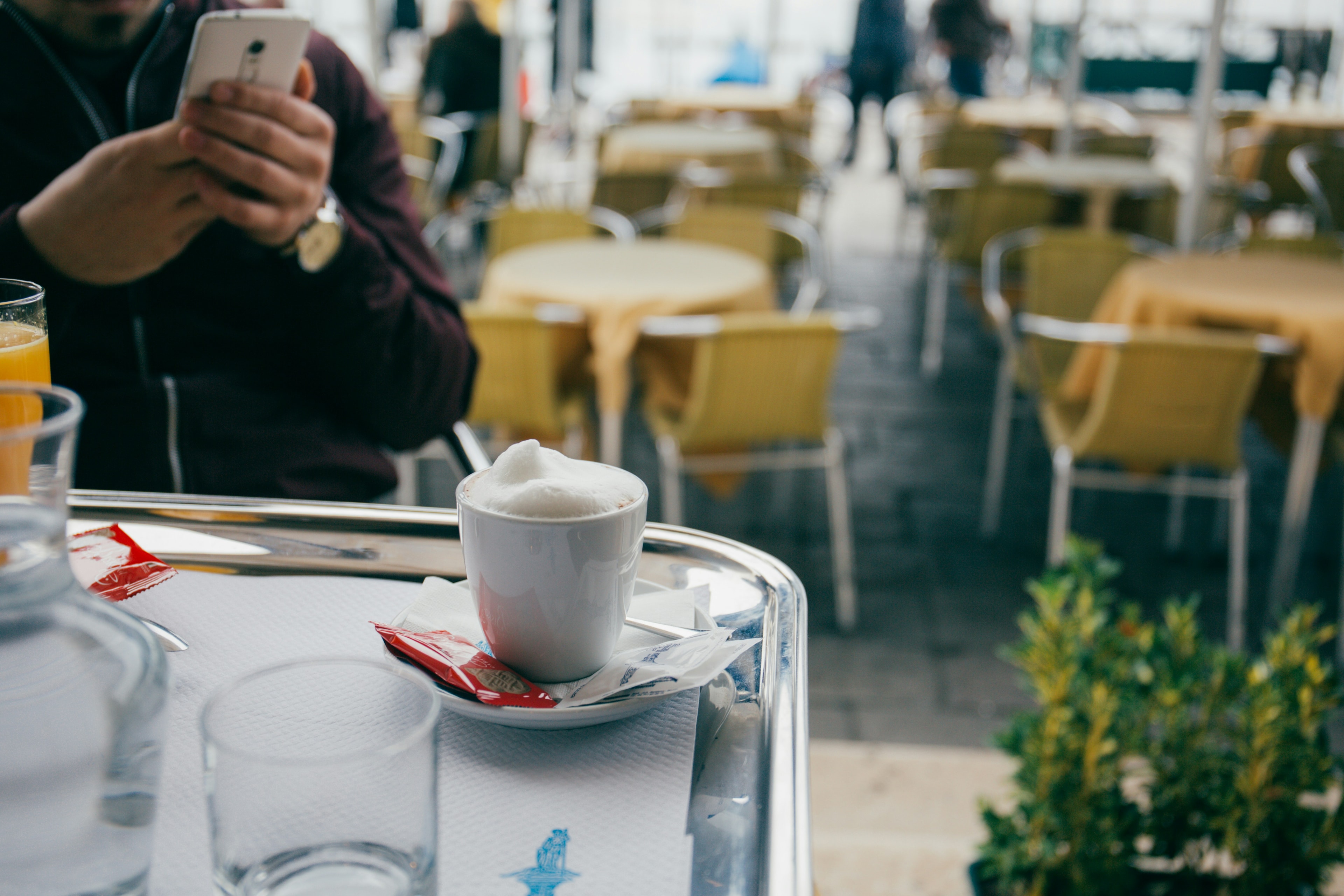 A person sitting at an outdoor cafe taking a picture of a cappuccino.