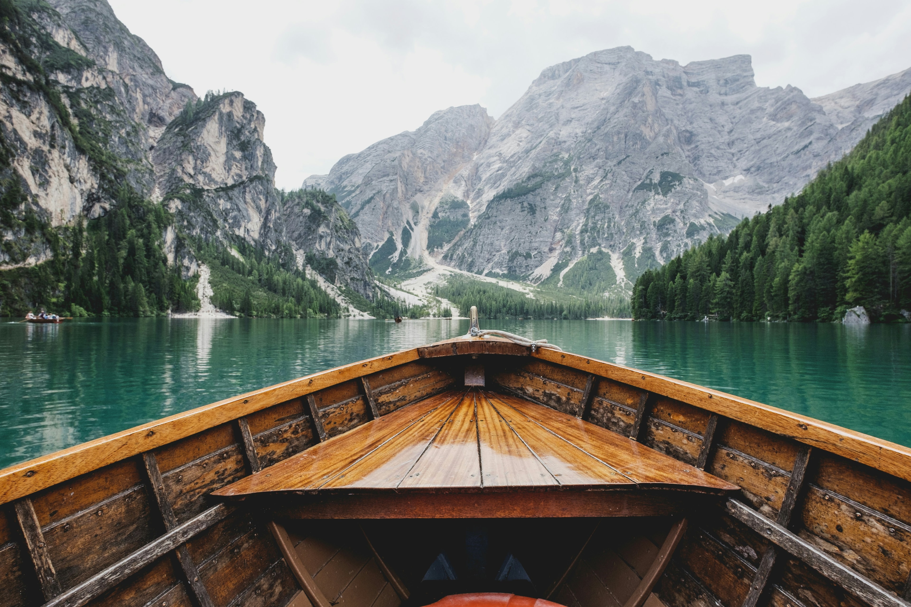 A point of view perspective from a wooden canoe-style boat on a turquoise river, revealing a sight of glorious mountains ahead.