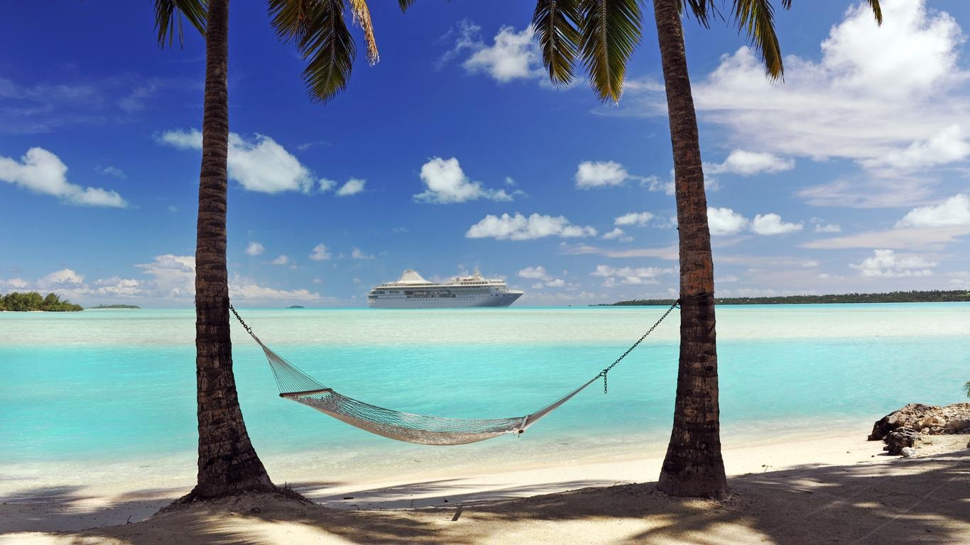 Two palm trees with a swing in between on the blue water beach.