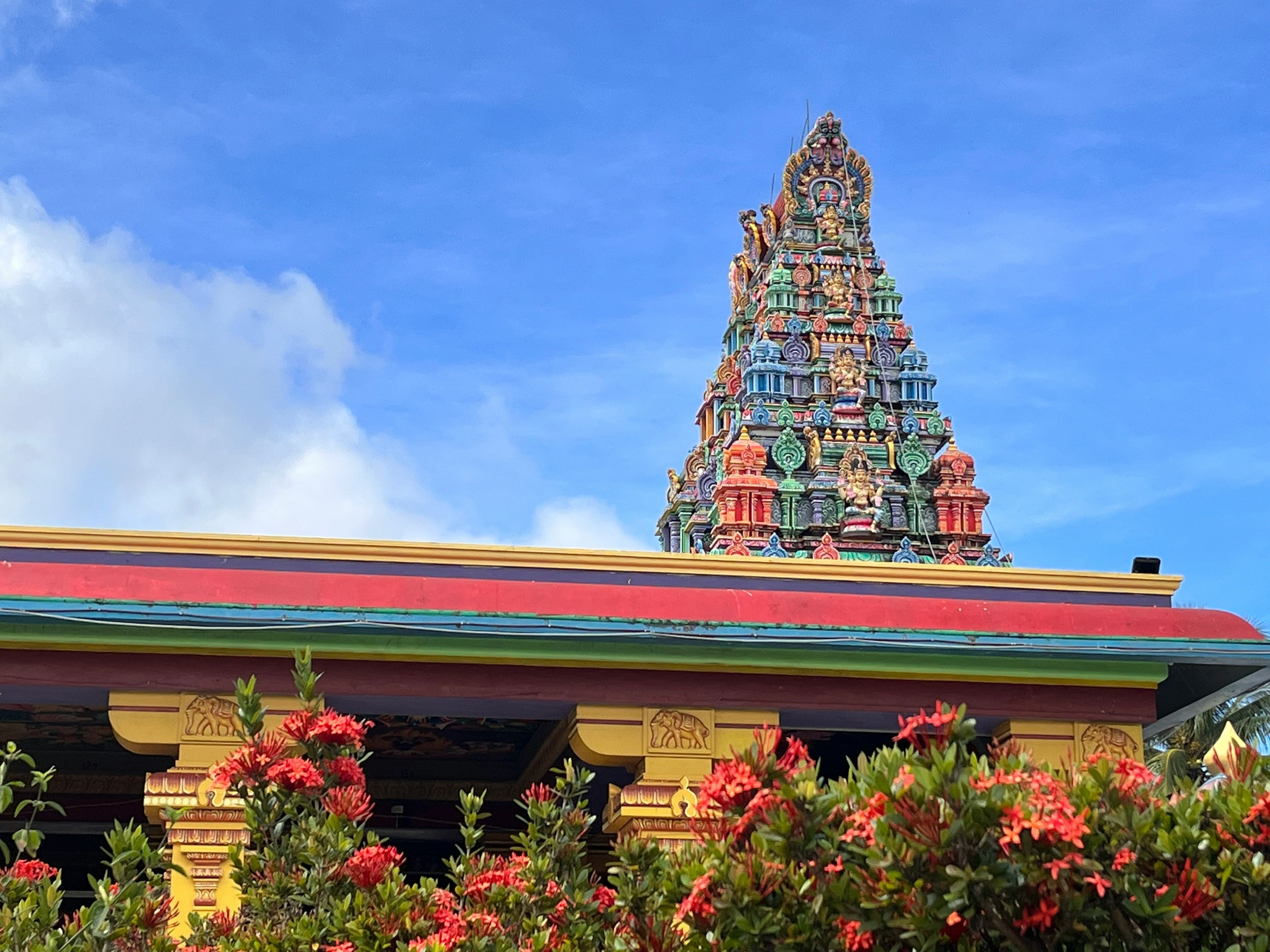 A colorful temple tower with intricate details, framed by green foliage and red flowers.