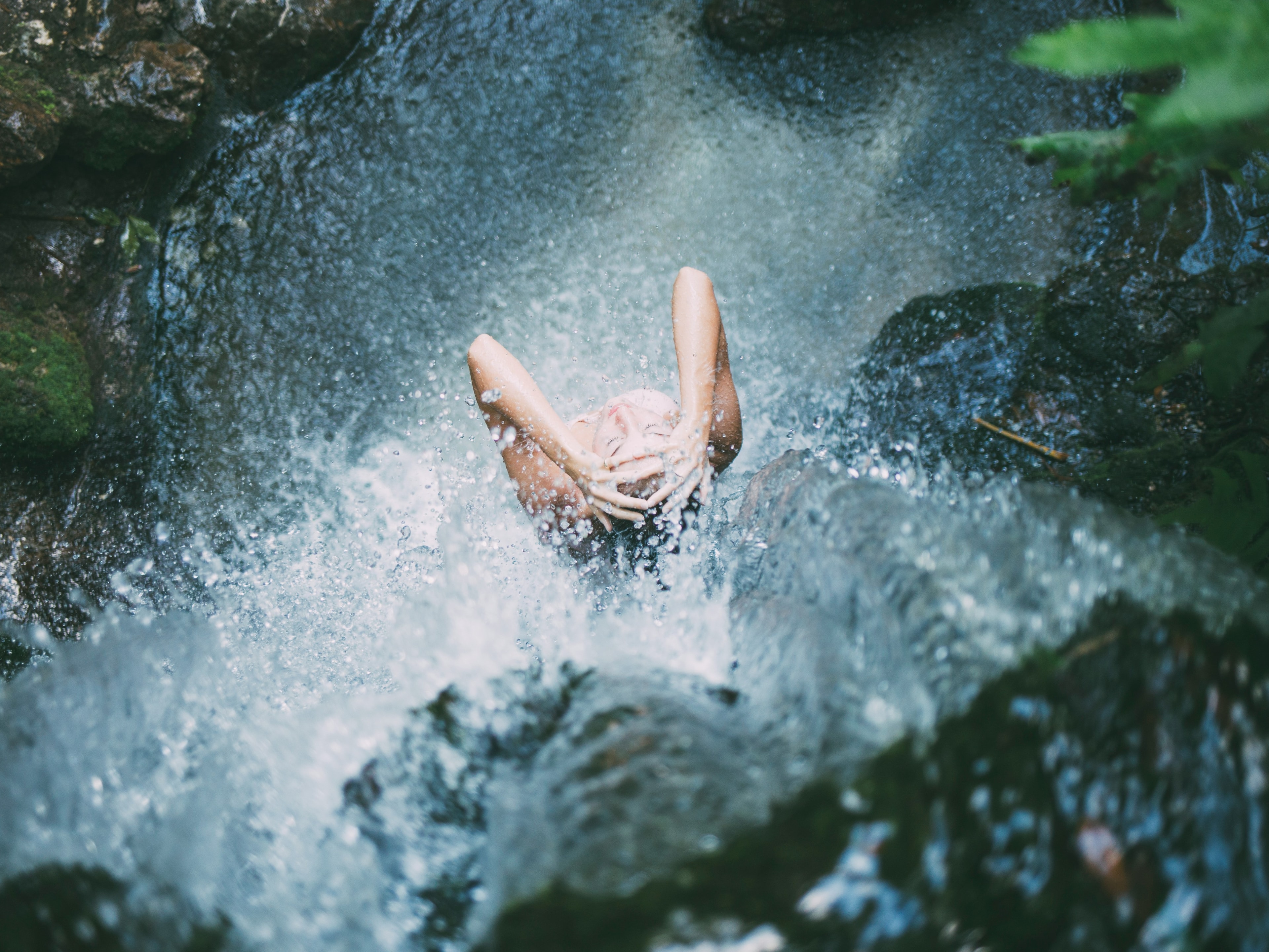 An overhead view of a person relaxing in a natural water body, surrounded by rocks and greenery.