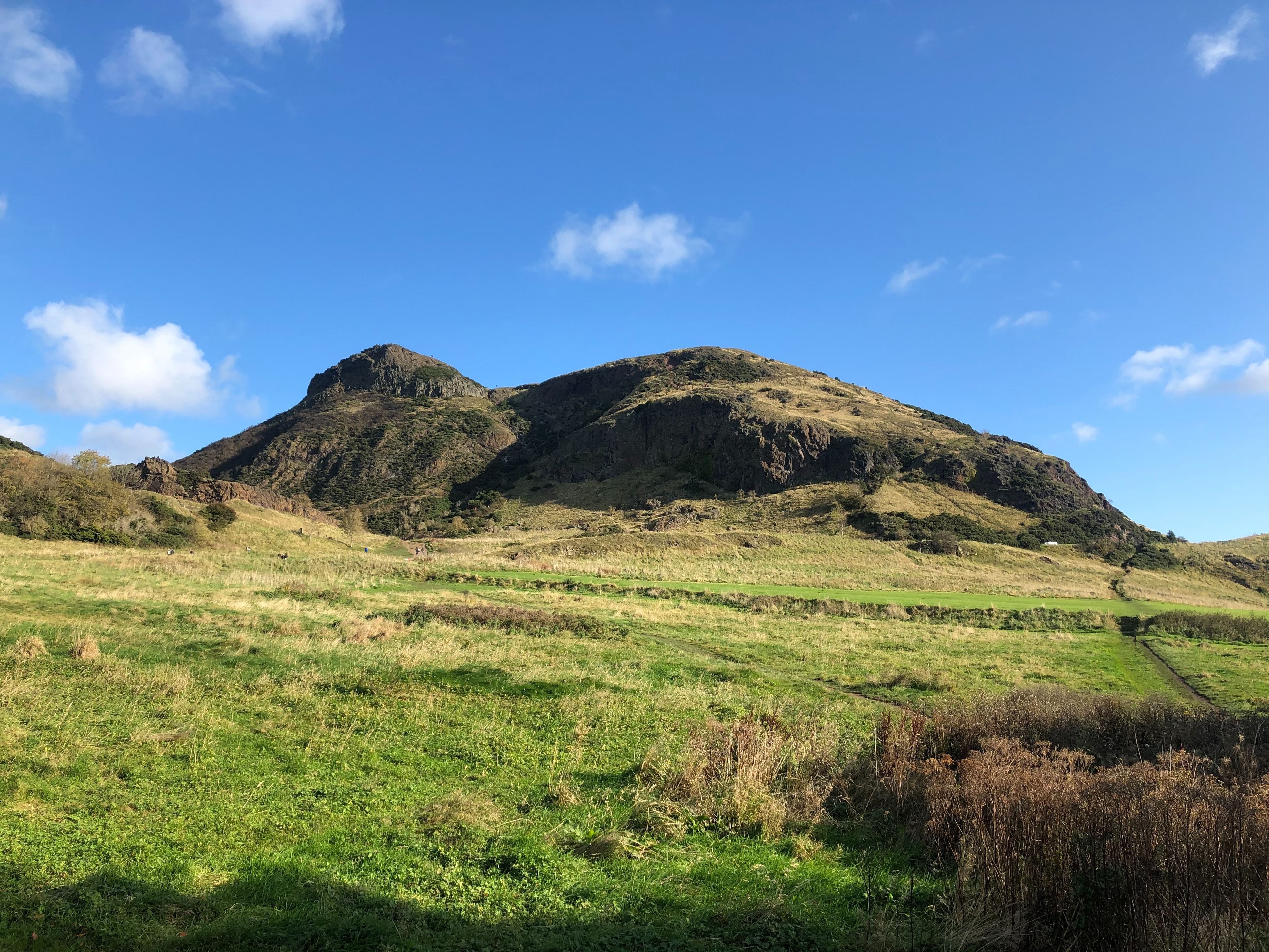 A picturesque landscape with a prominent hill, a grassy field, and a clear blue sky.