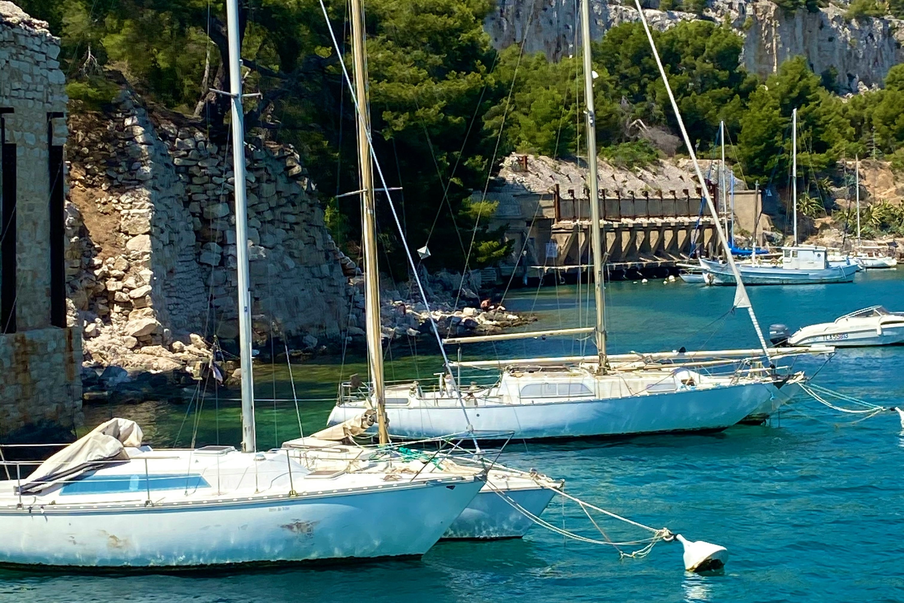 A few sailboats docked in the water at Calanques National Park, on a sunny day.