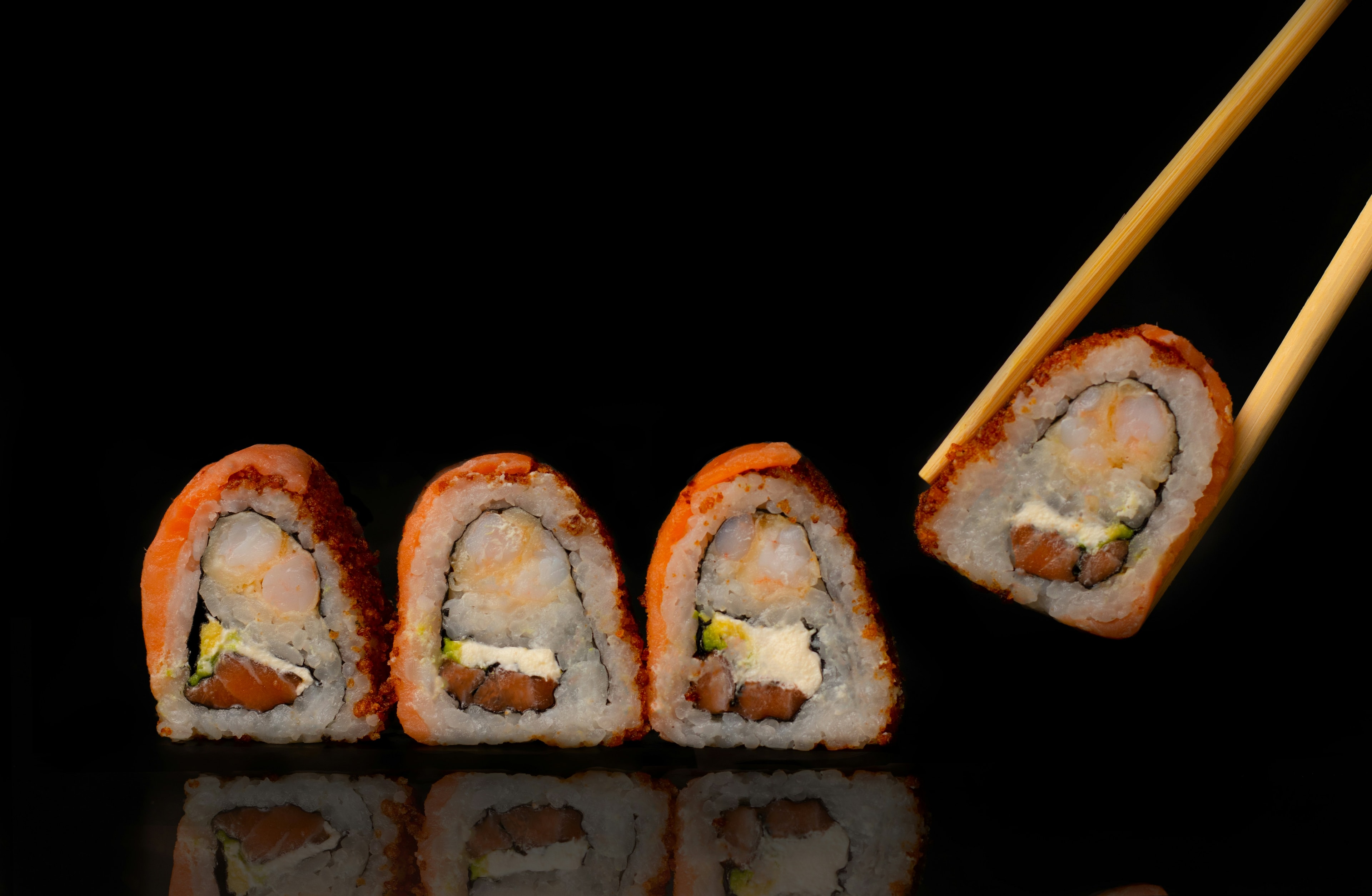 Sushi on a black background with one piece being picked up by chopsticks