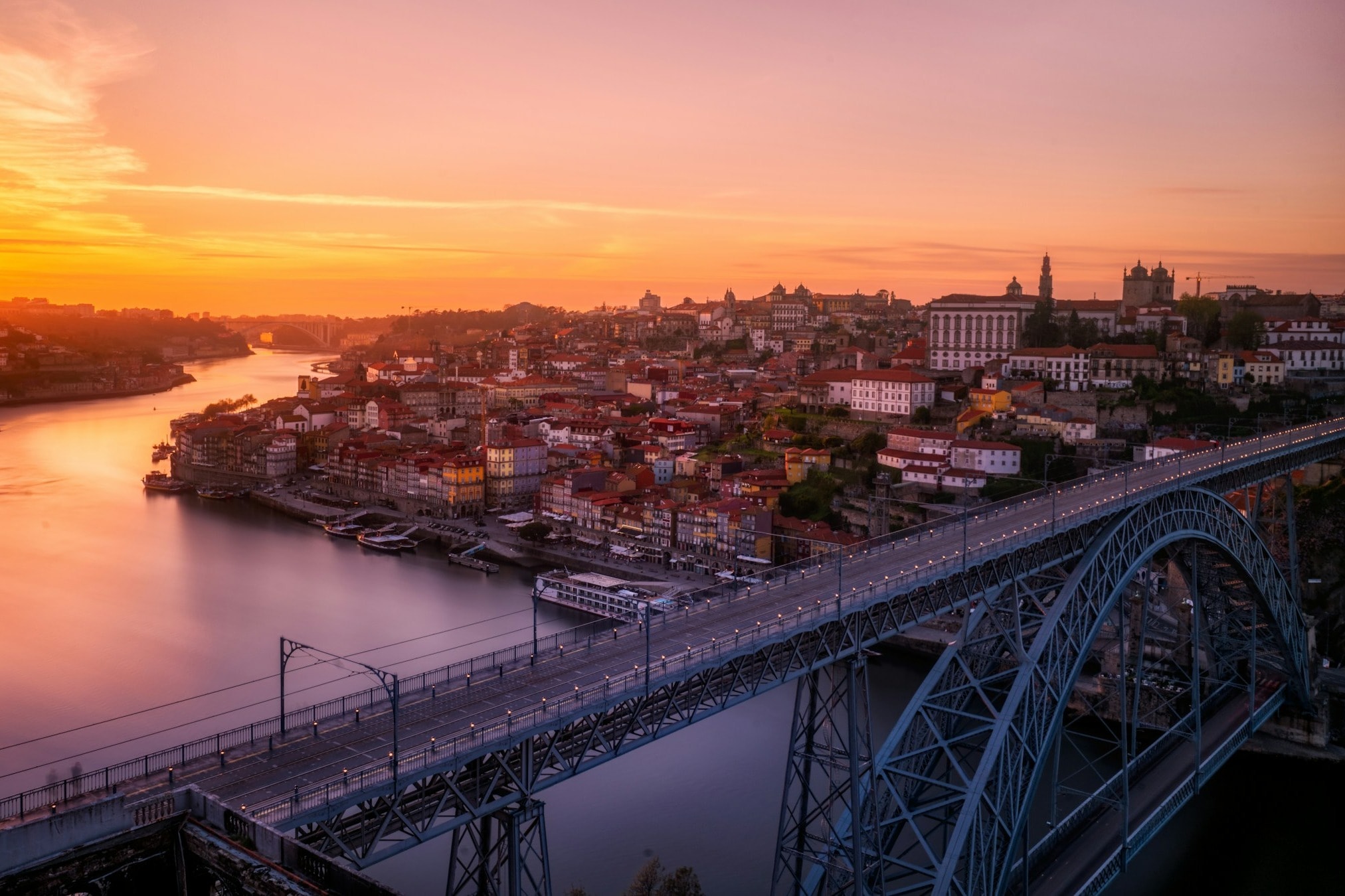 An aerial view of The Douro River, coastline, skyline  and bridge in Porto, beneath a golden sunset.