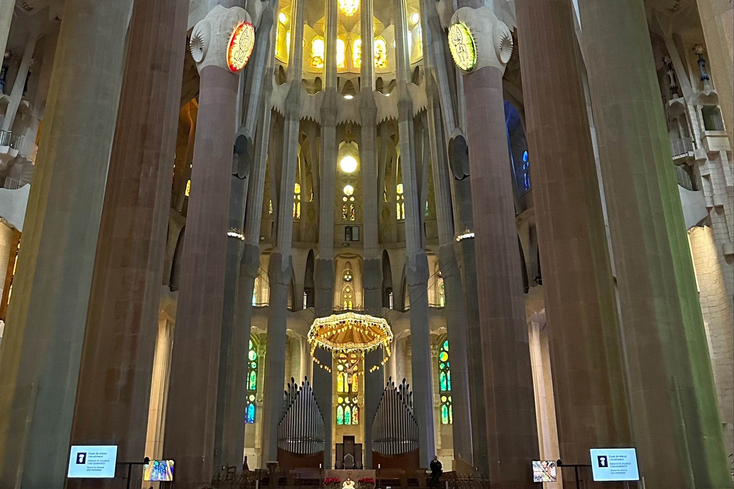 Inside La Sagrada Familia, showing a central illuminated altar with high ceiling