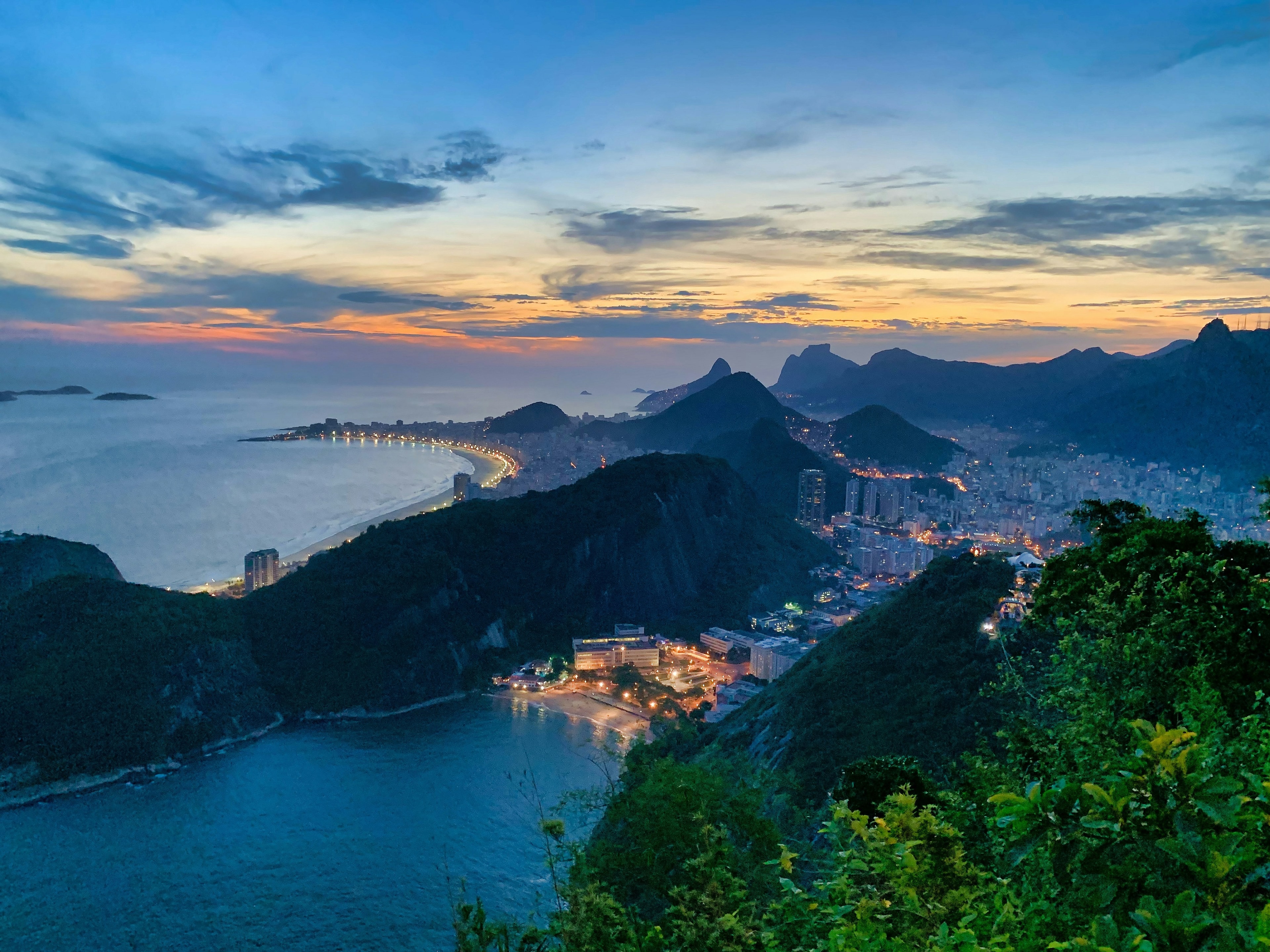 The image showcases the stunning cityscape of Rio de Janeiro at dusk, with the city lights twinkling against the backdrop of its famous mountainous skyline.