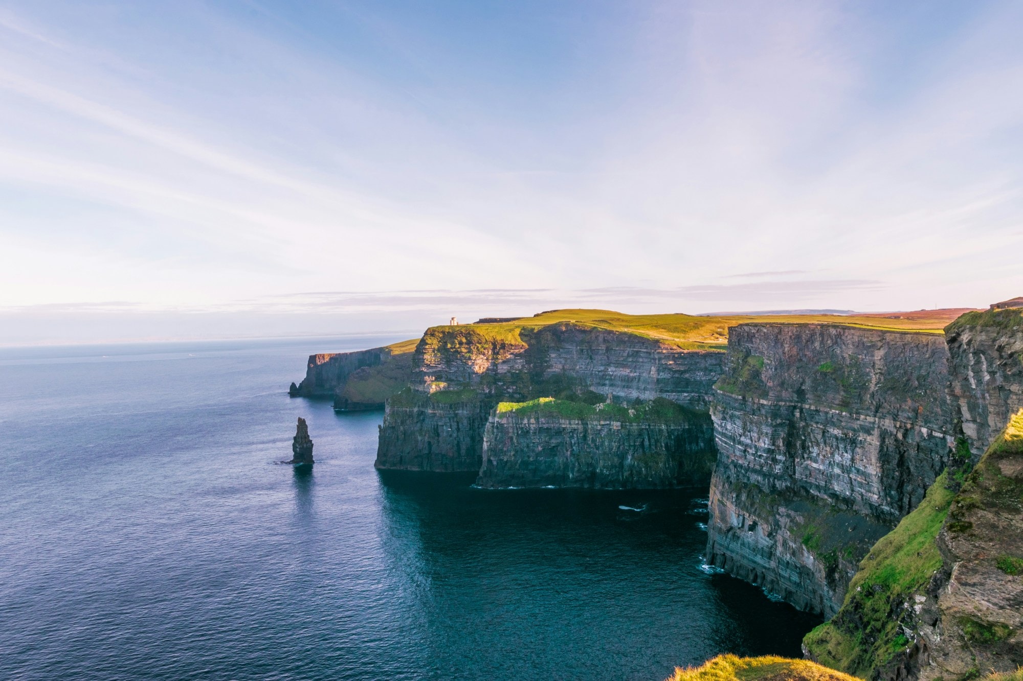 Dramatic cliffs with the sun shining onto the grassy landscape and calm ocean below