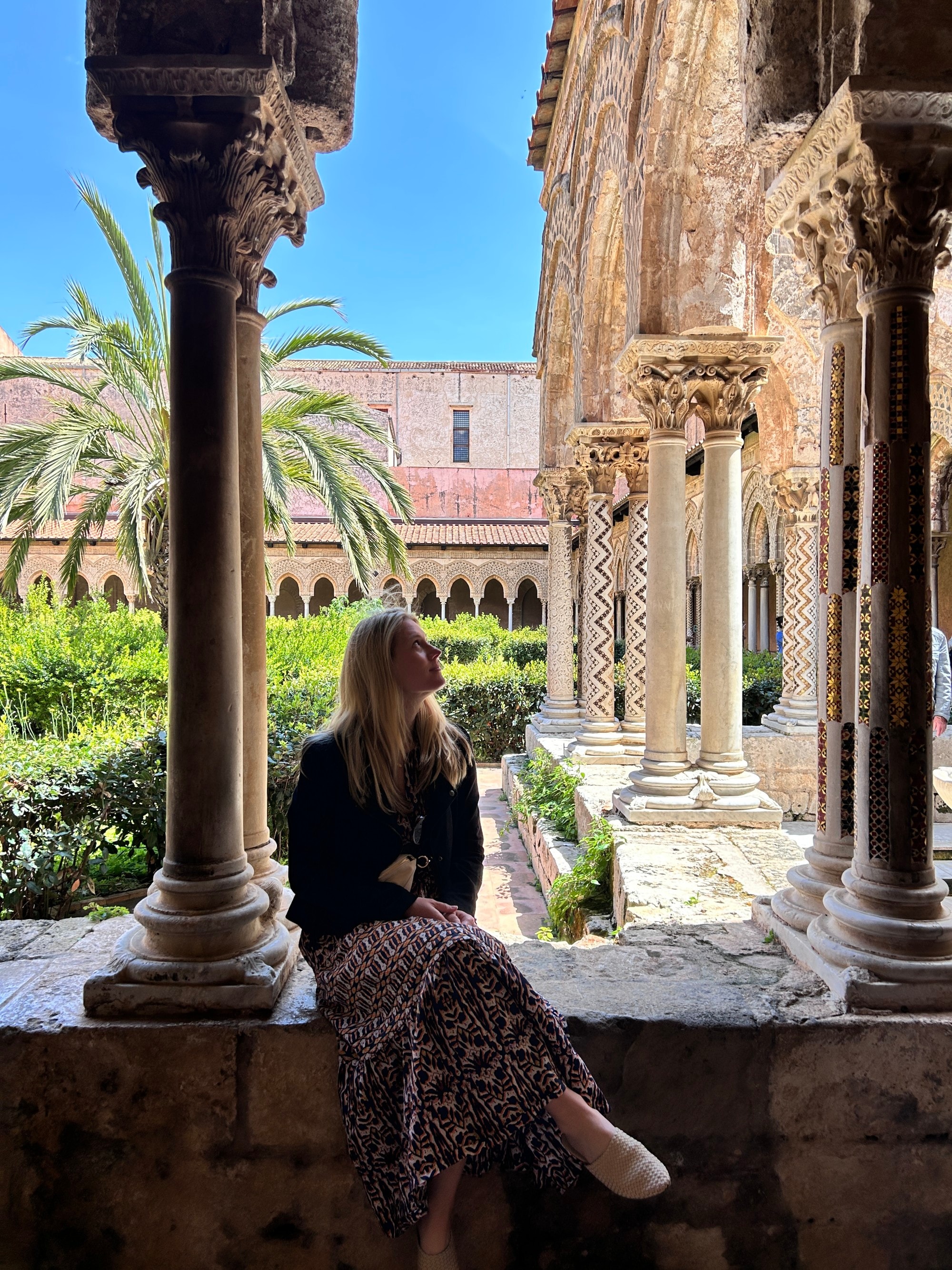 A woman sitting in a veranda with pillars.