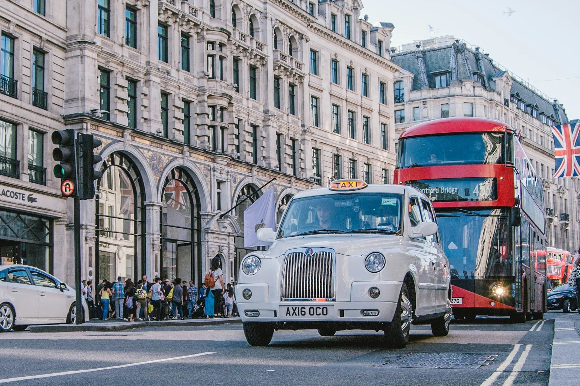 A white taxi in front of a red double-decker bus on the road