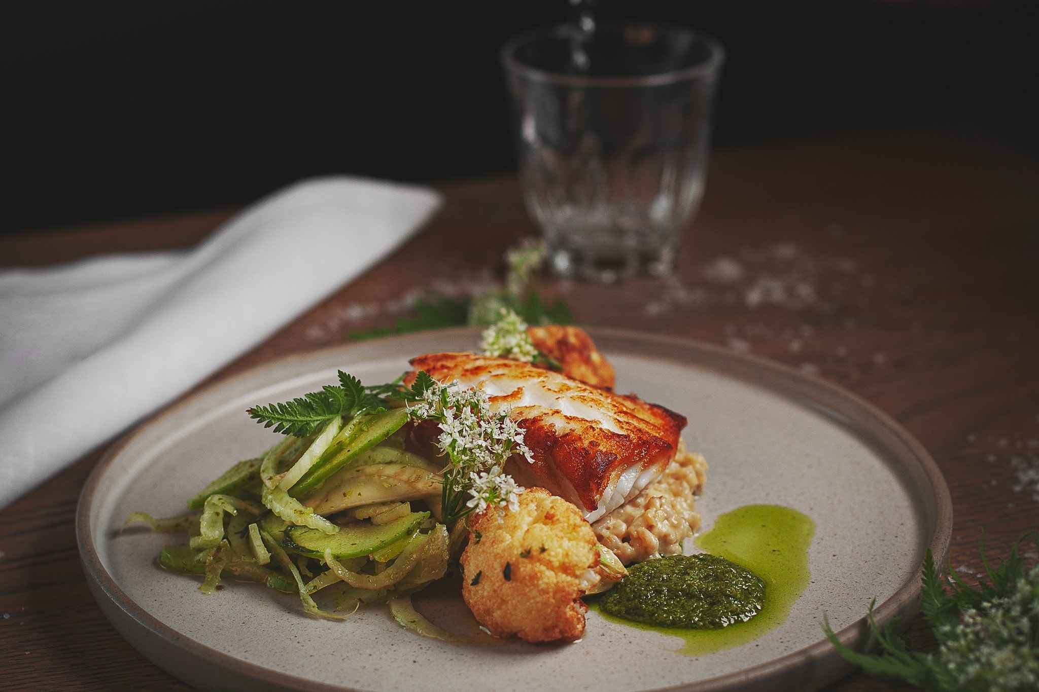 A delish-looking plat of food from Matur og Drykkur, composed of pan-seared fish over a bed of rice-pilaf, a green salad, rustic cauliflower and a green sauce.