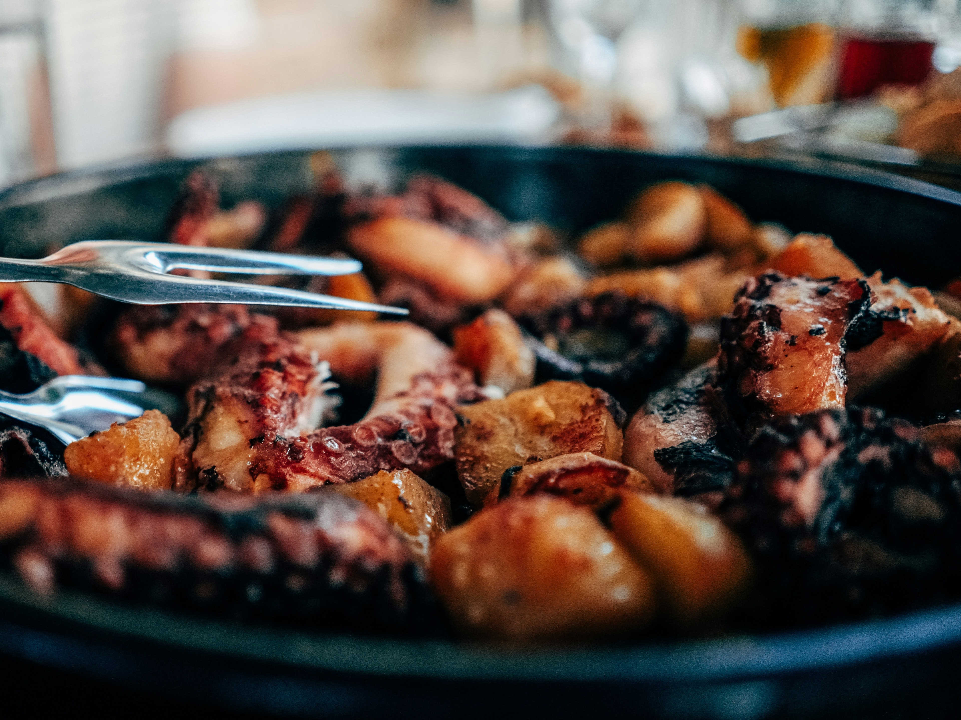 A close-up of grilled meat and vegetables in a pan, with tongs picking up a piece.