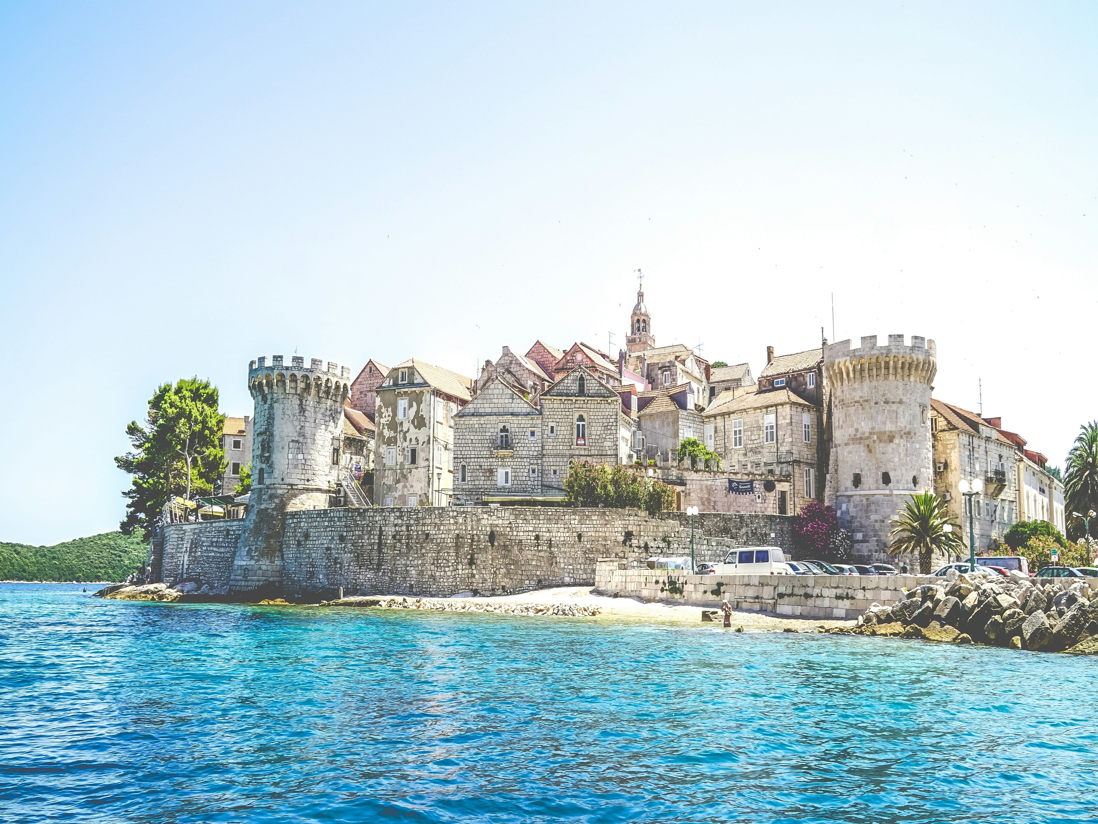 A scenic coastal town with ancient stone buildings and fortifications under a clear blue sky.