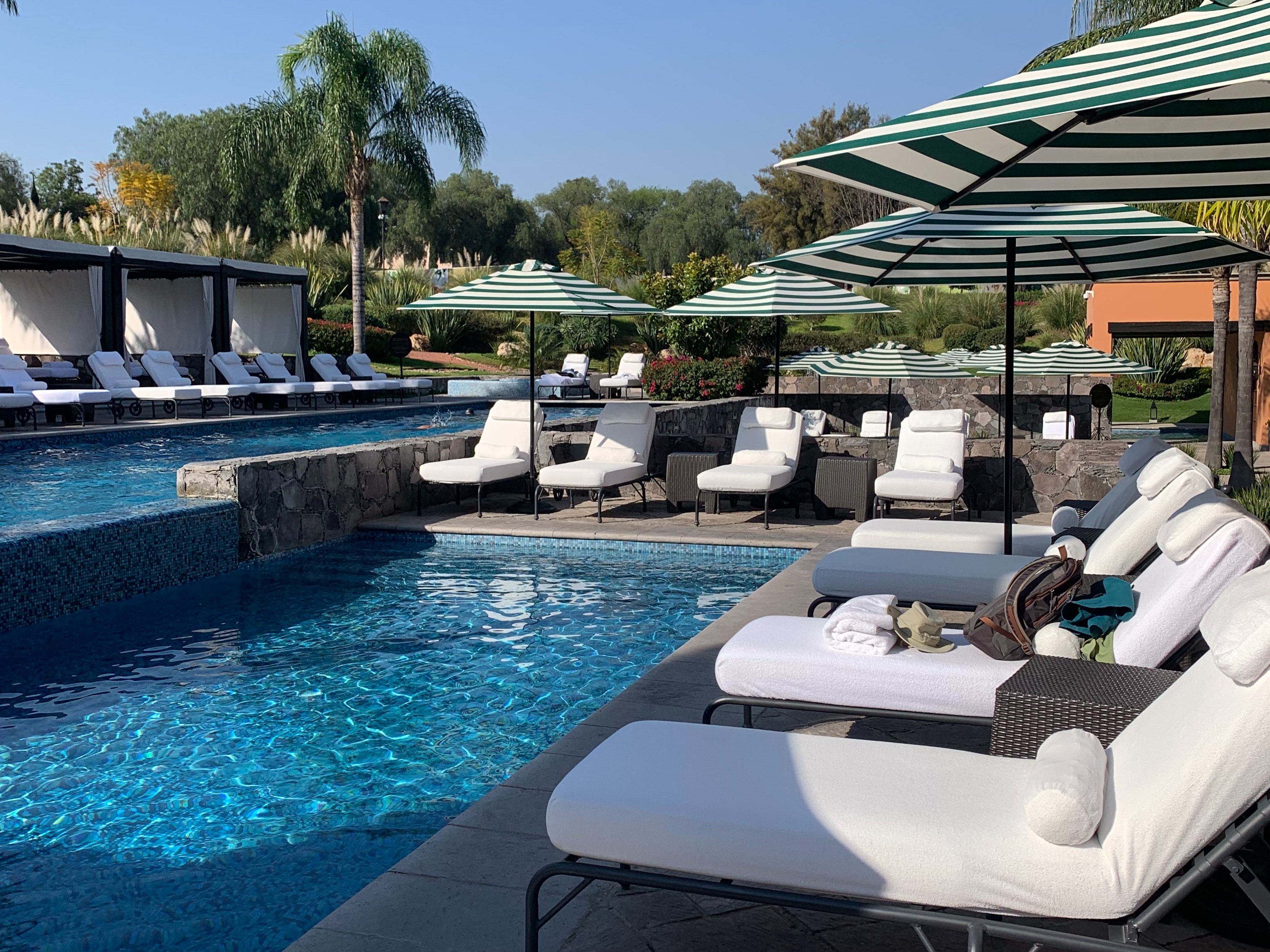 Duplex pool area of a resort with white sun loungers and green and white striped umbrellas