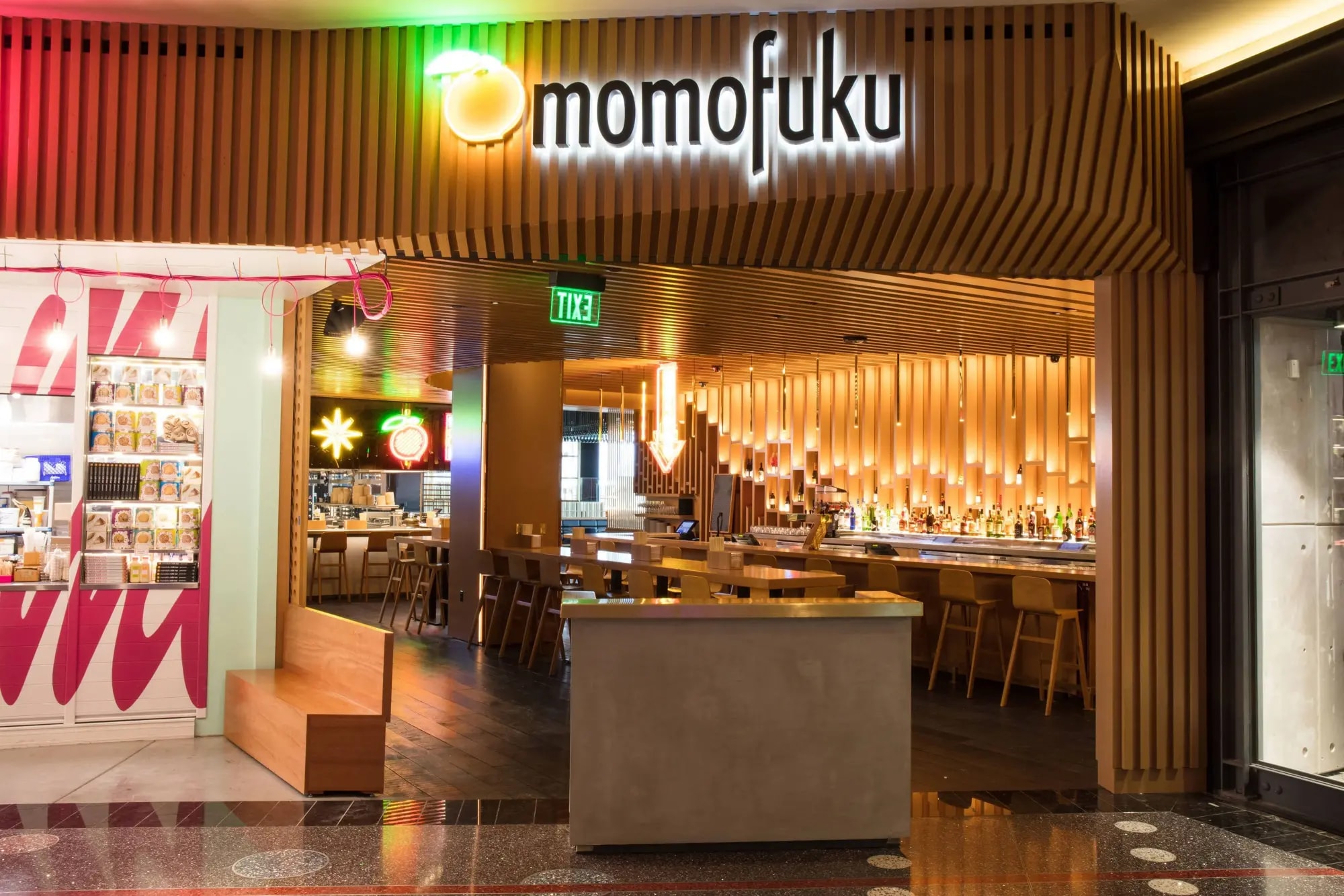 a hotel restaurant with pale-wood furniture and a clean aesthetic, with a lit sign that reads "momofuku"