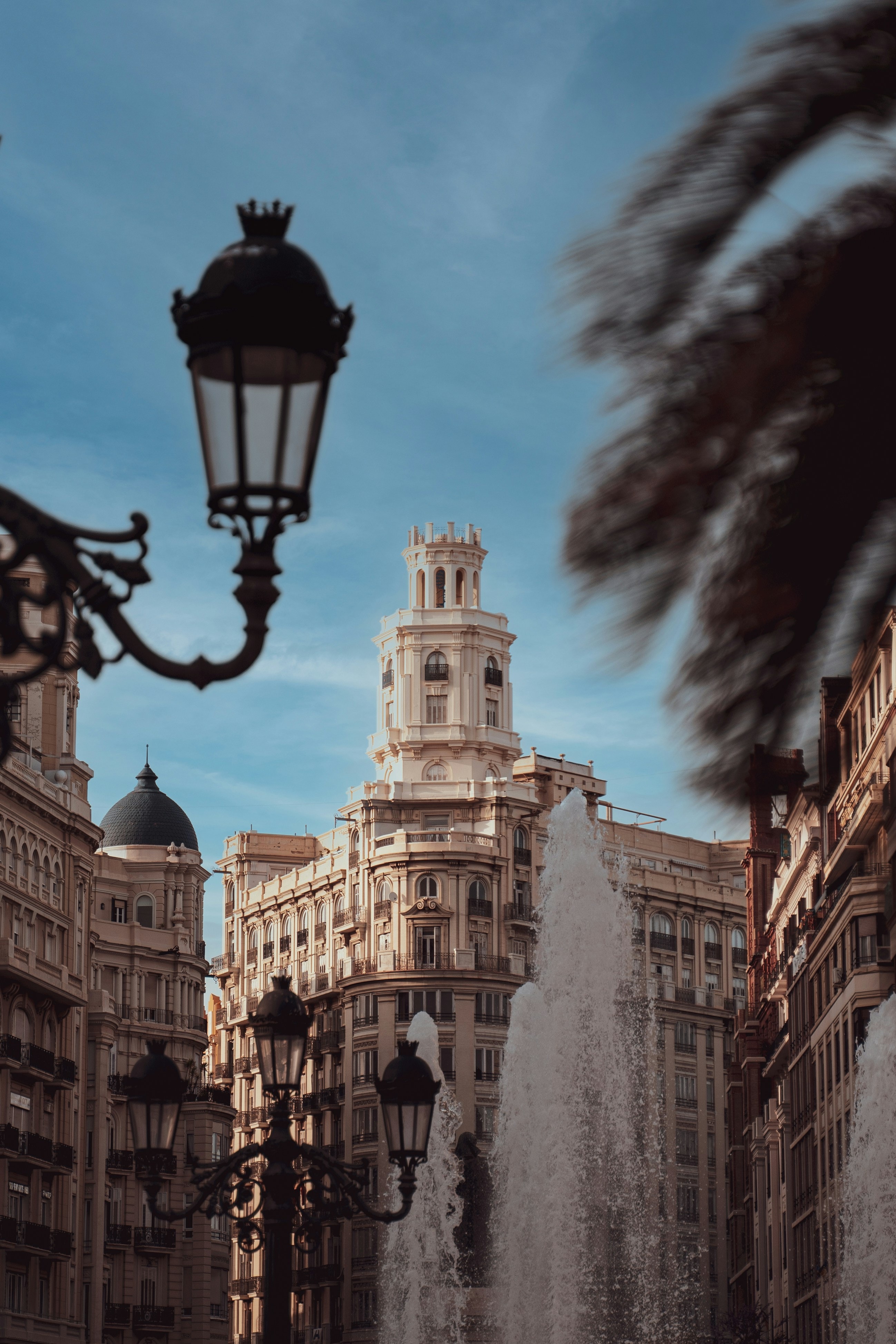 A look at Valencia's classic architecture, with the spouted water of a fountain and street lamp in front.