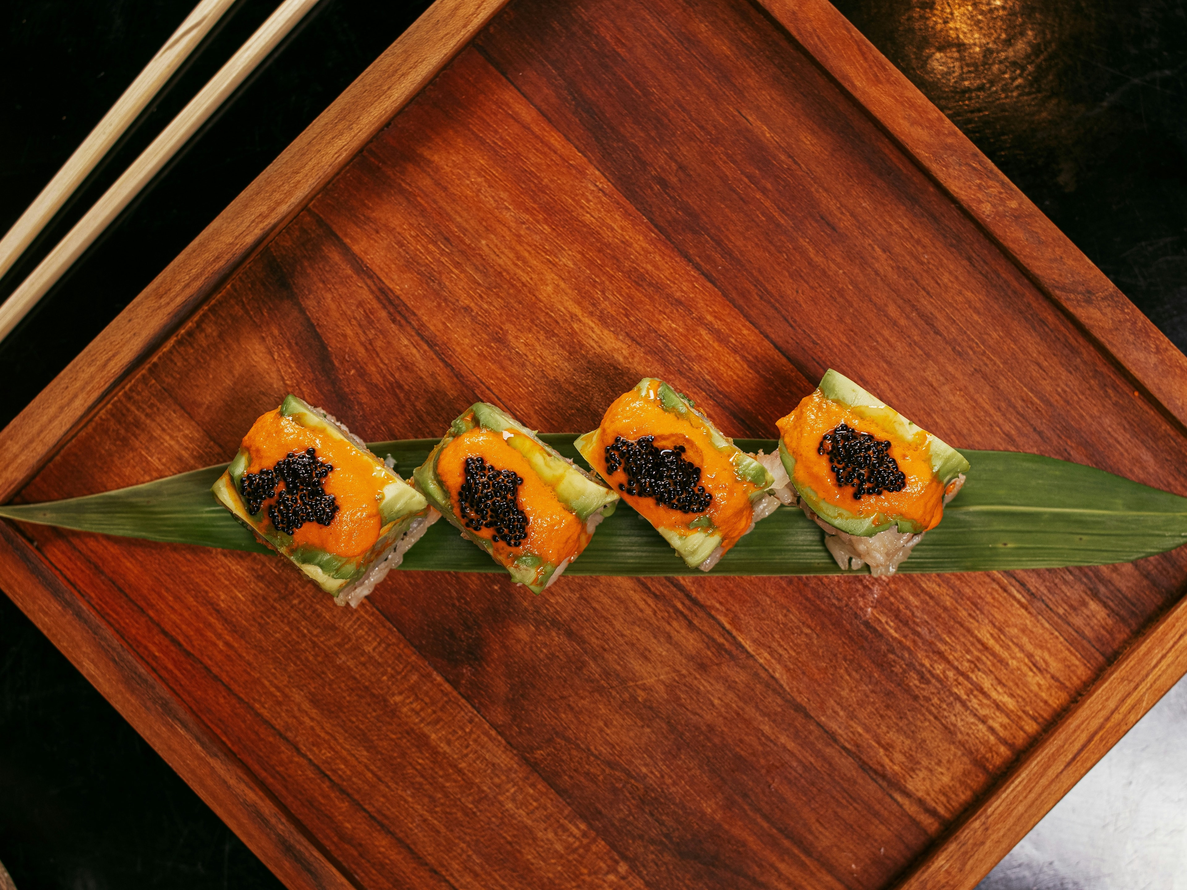 A sushi arrangement on a bamboo leaf on top of a wooden table.