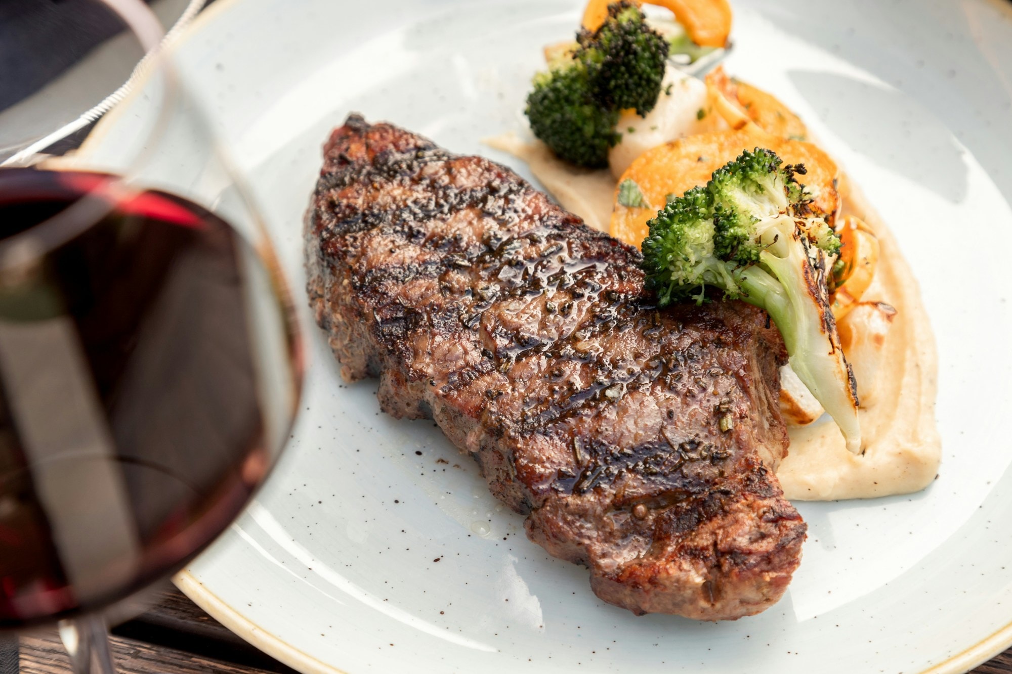 Steak, mashed potato and broccoli on plate with wine.