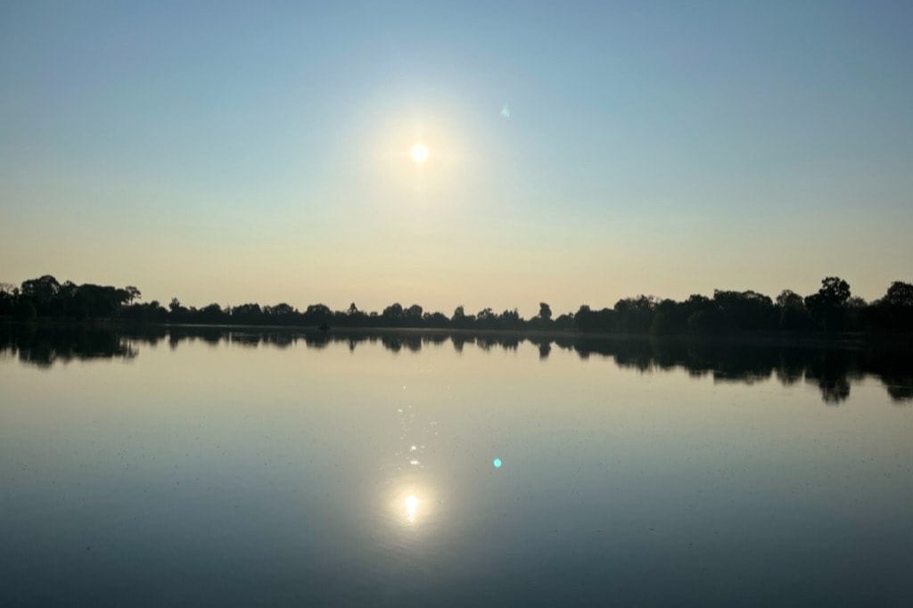 A peaceful sunset over a still lake, with the sun’s reflection creating a path of light across the water.