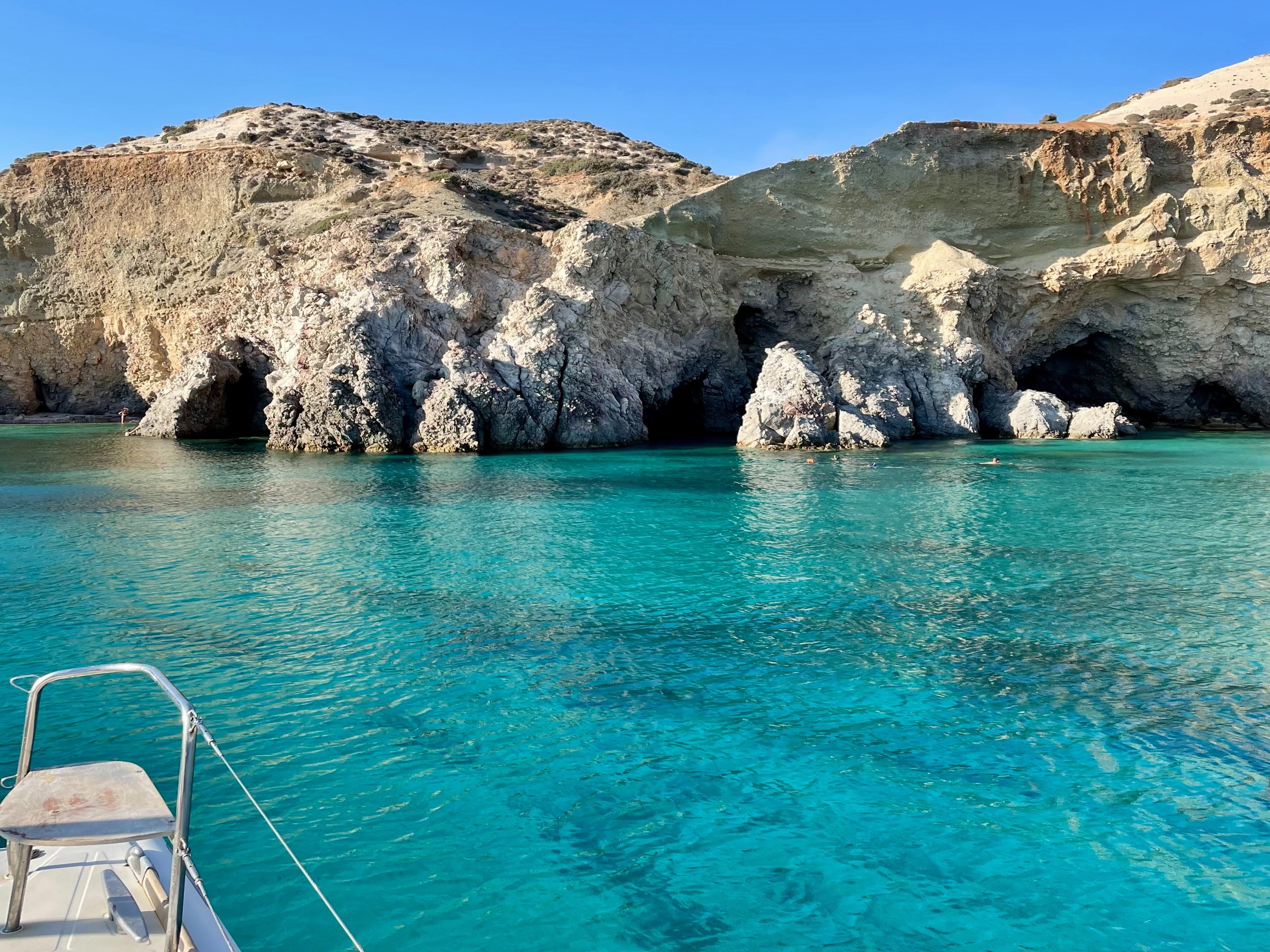 A view of beach caves from a boat tour, in the clear, turquoise sea on a sunny day in Milos, Greece. 