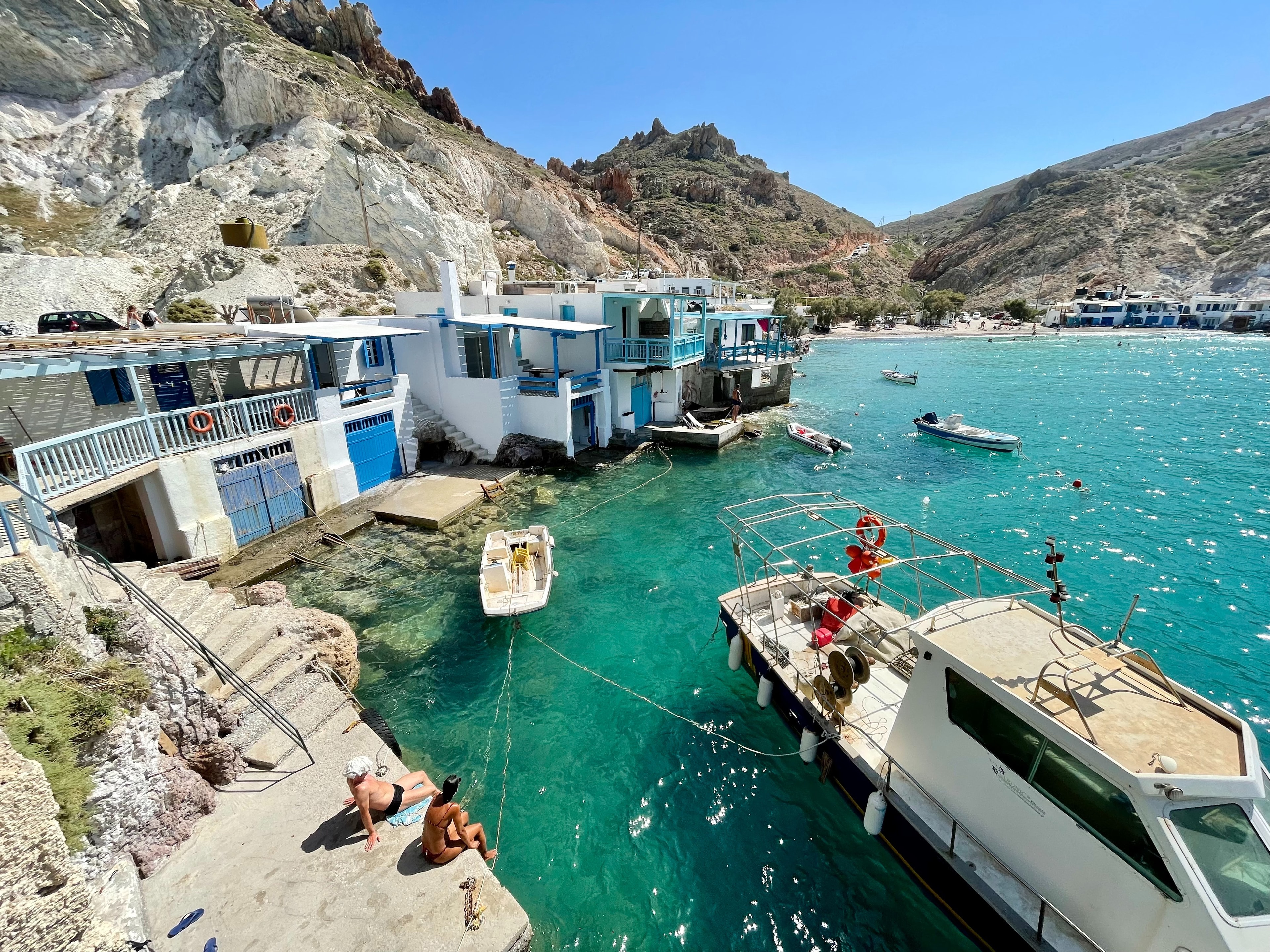 A small fishing harbor on a sunny day, and small houses tucked between rocky cliffs.