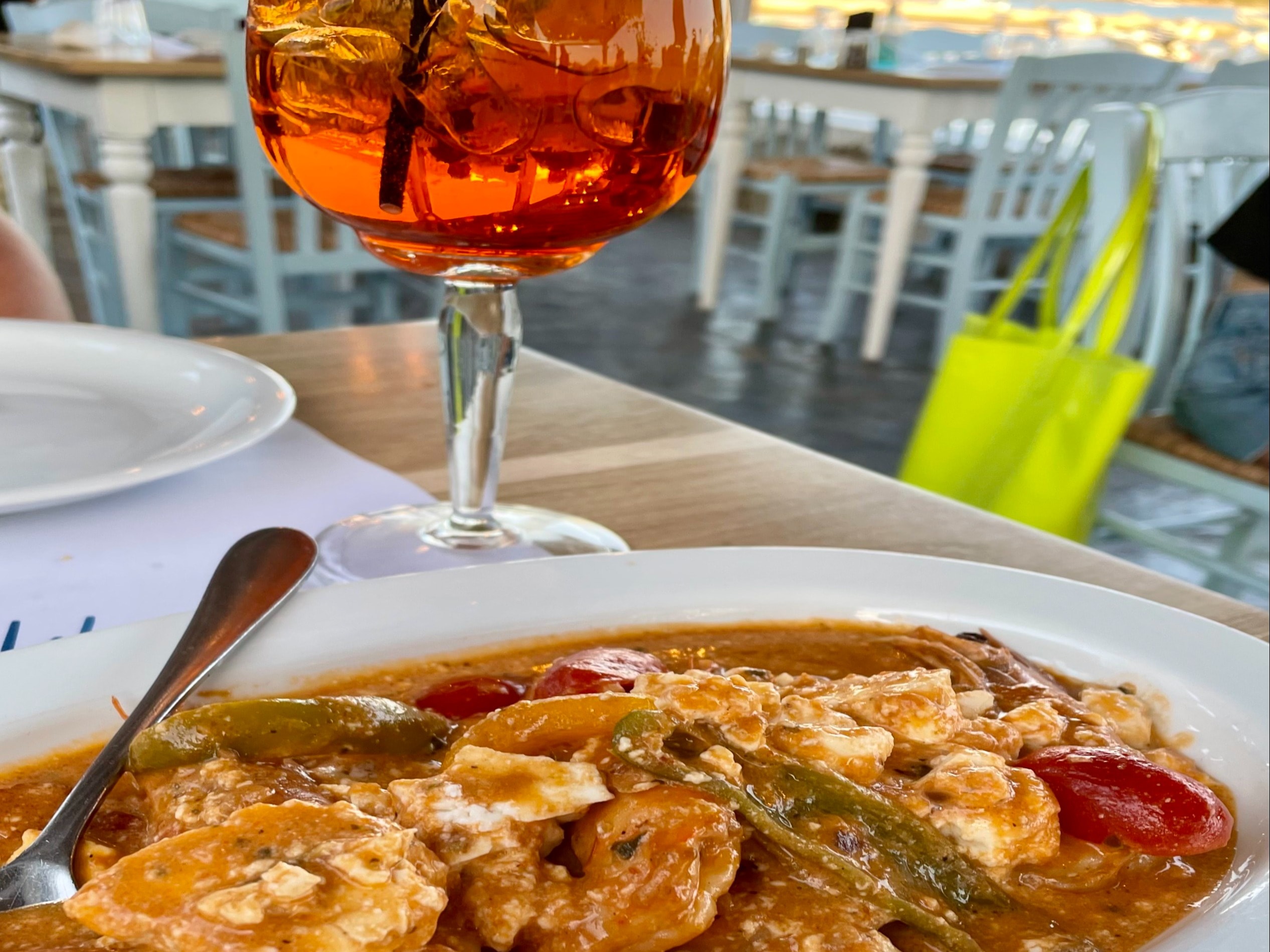 A traditional Greek plate of shrimp saganaki and a cocktail at an outdoor restaurant in Milos, Greece.