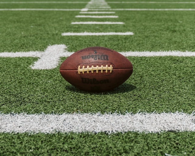 A brown football laying on a green football field