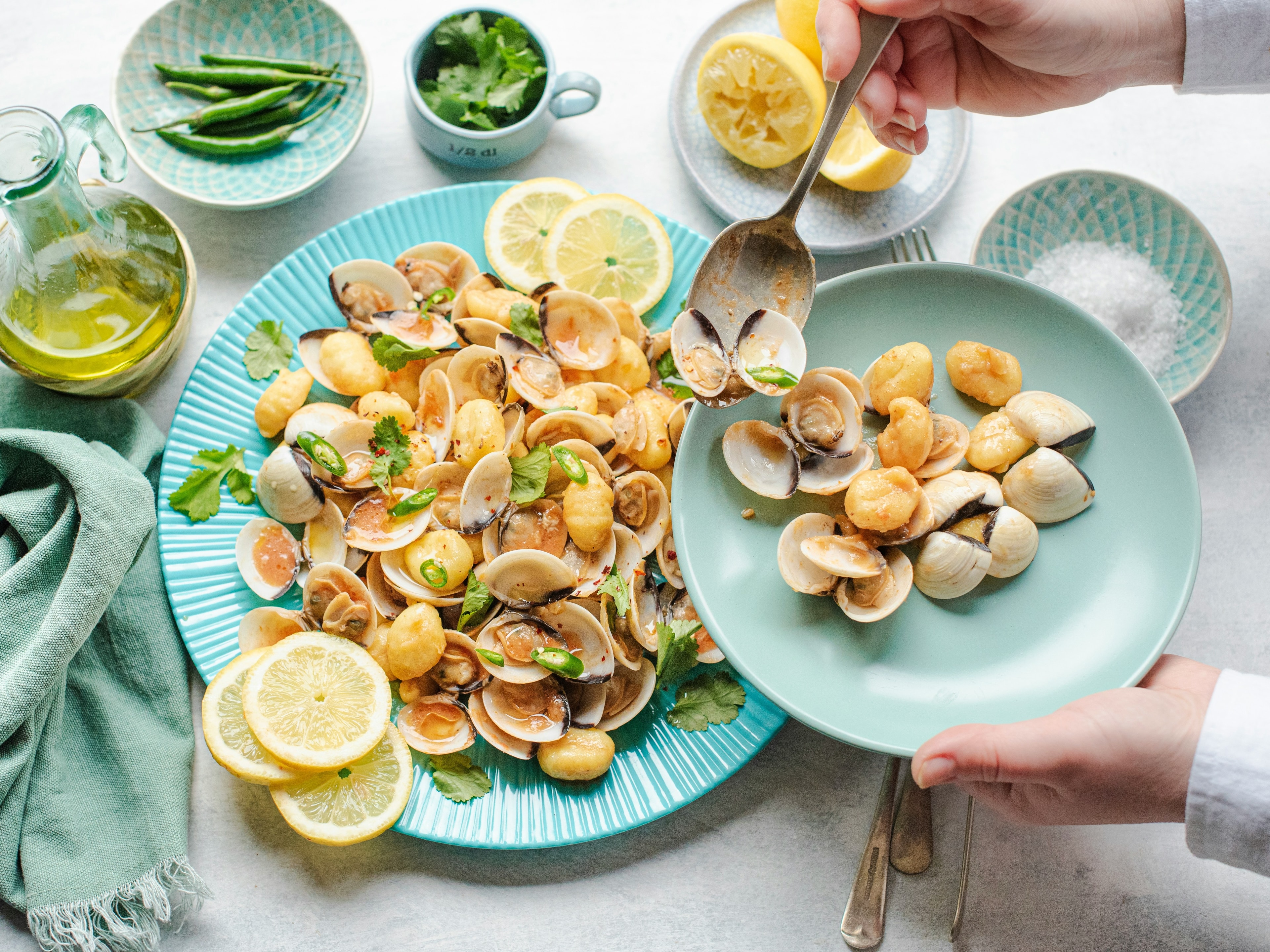 A platter of cooked clams served with lemon and chilies on a table on green and blue dishes