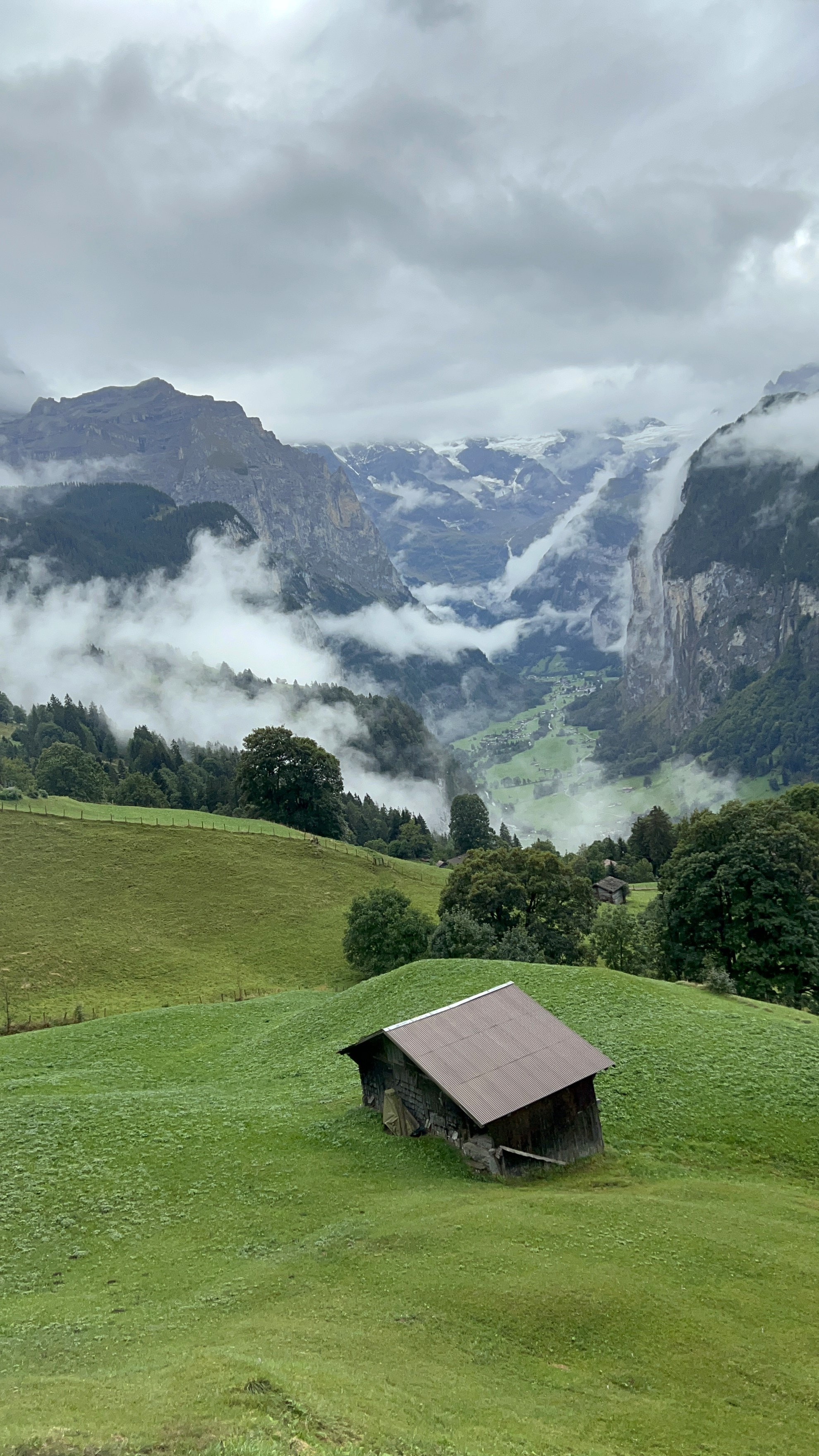 Beautiful view of the mountains with low clouds around and a small brown house on a grassy hill