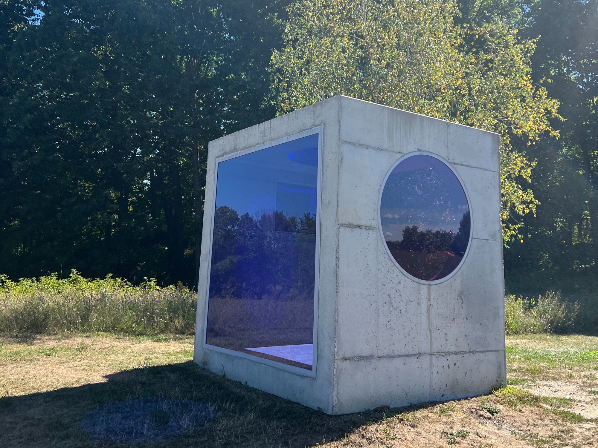 A square grey sculpture outdoors with round and square windows. 