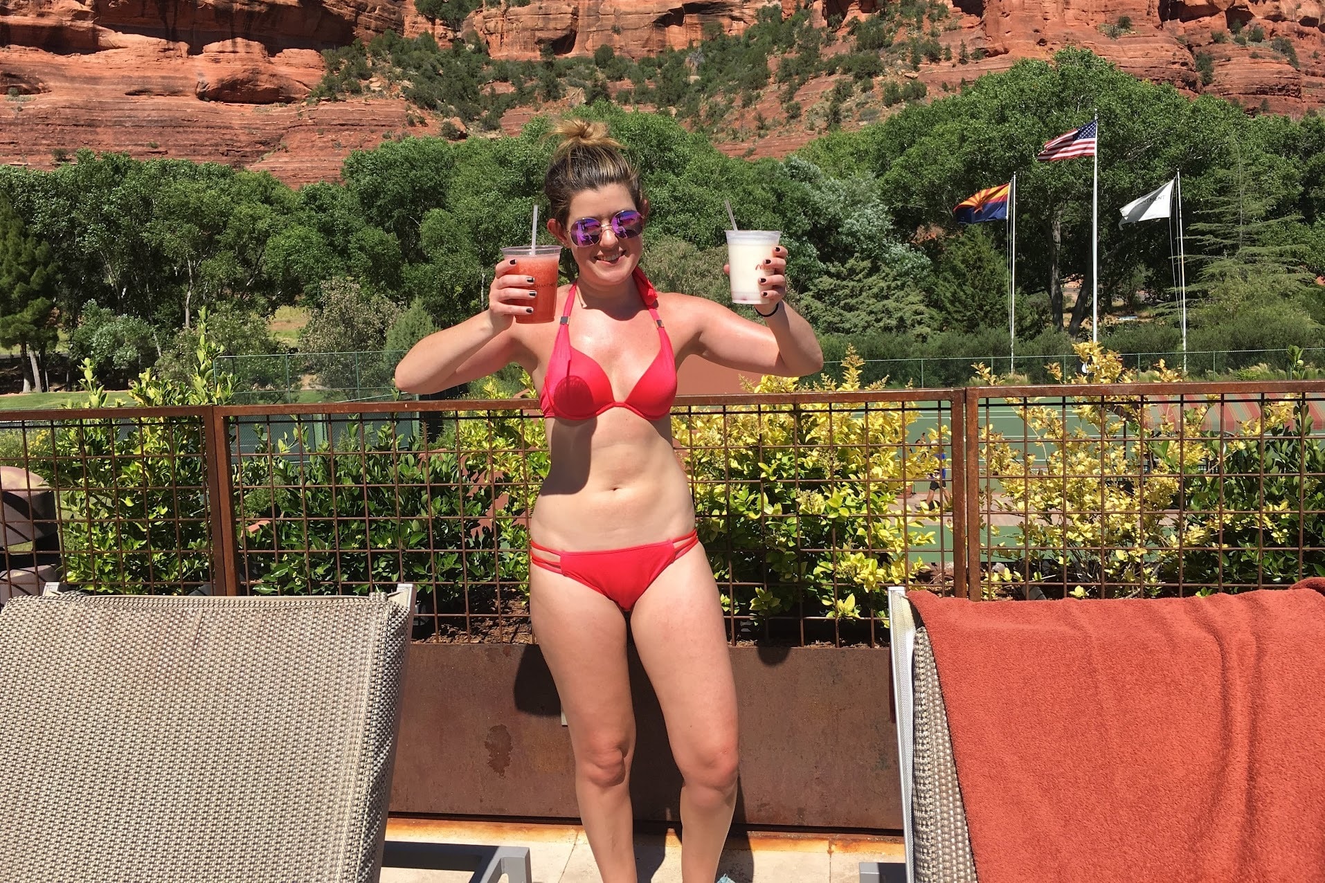 A picture of a person wearing shades and holding smoothies near a mountainous area during the daytime.