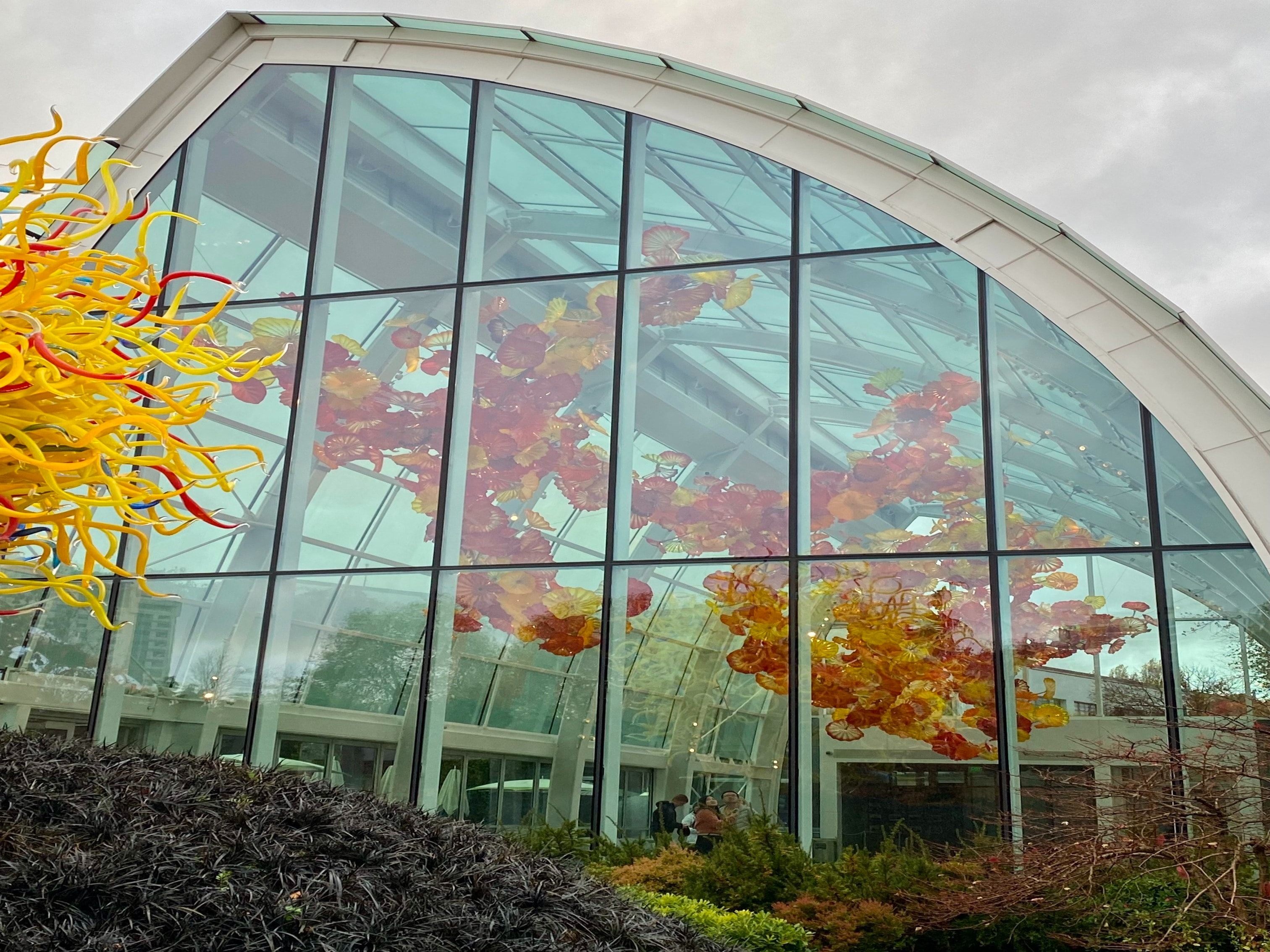 A large building with an arched set of windows. There is sculptural artwork and bushes in the surrounding areas. 